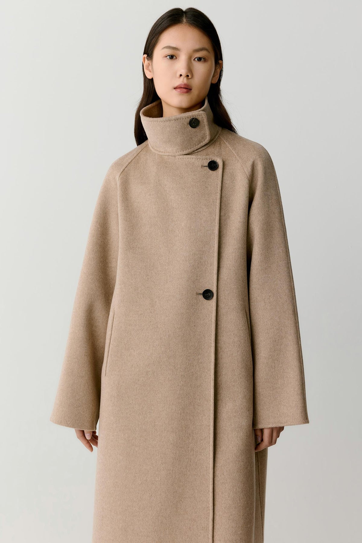 Three-quarter view highlighting the long cut, raglan sleeves and structured drape of the natural beige double-face cashmere coat.