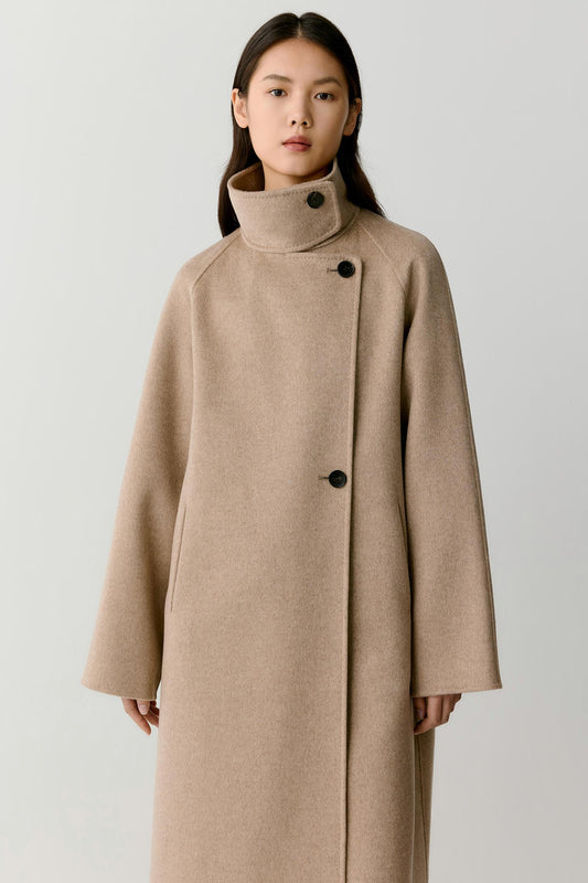 Three-quarter view highlighting the long cut, raglan sleeves and structured drape of the natural beige double-face cashmere coat.
