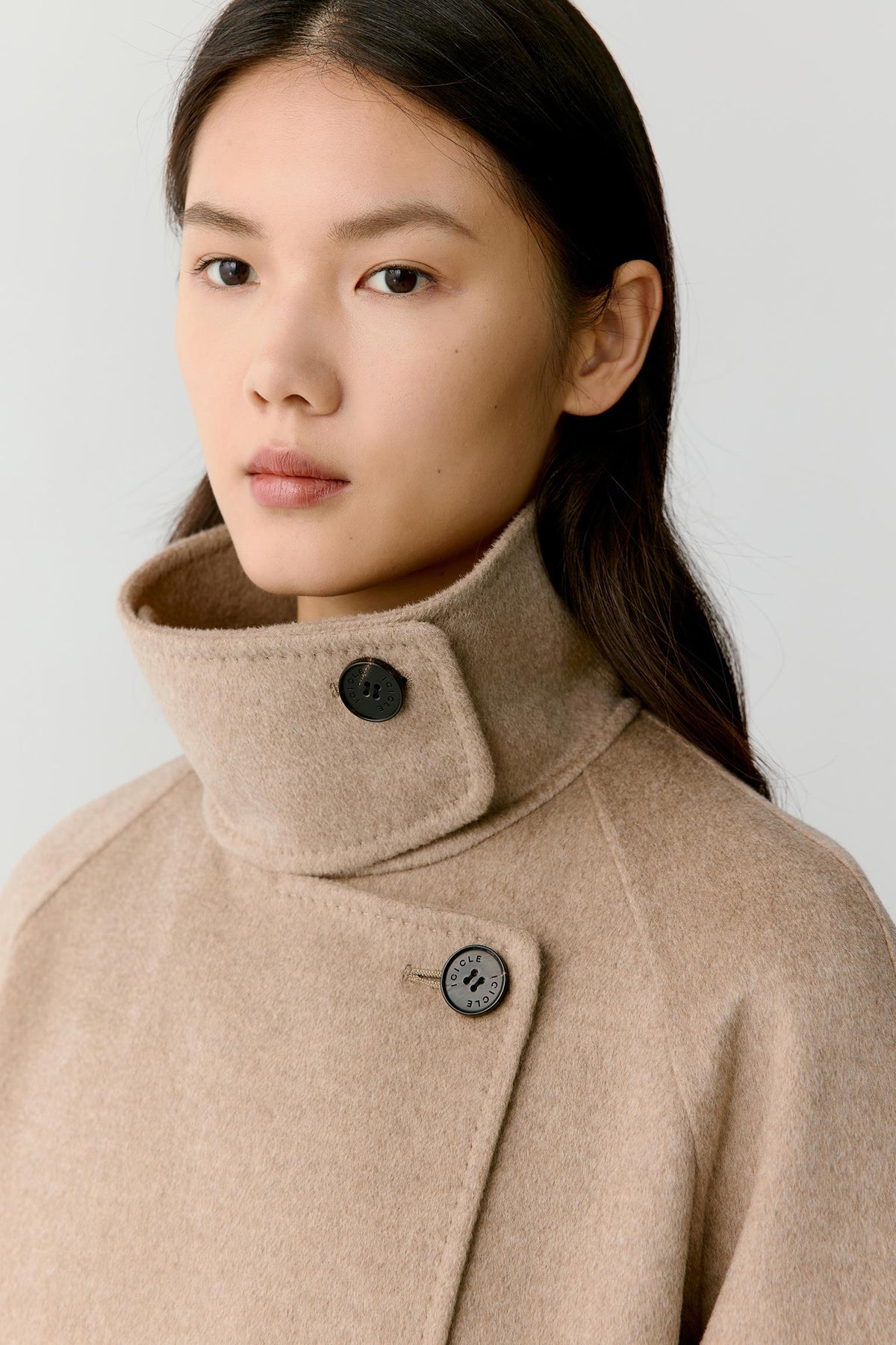 Close-up highlighting the high stand collar, asymmetric button fastening and soft natural beige cashmere surface.