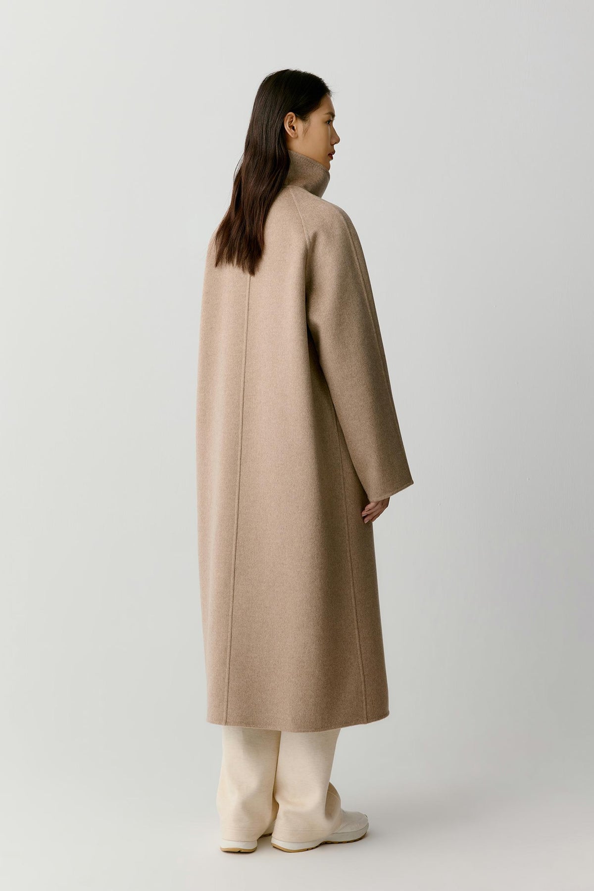 Side view of a woman wearing the natural beige double-face cashmere coat, showing the long silhouette and clean construction.