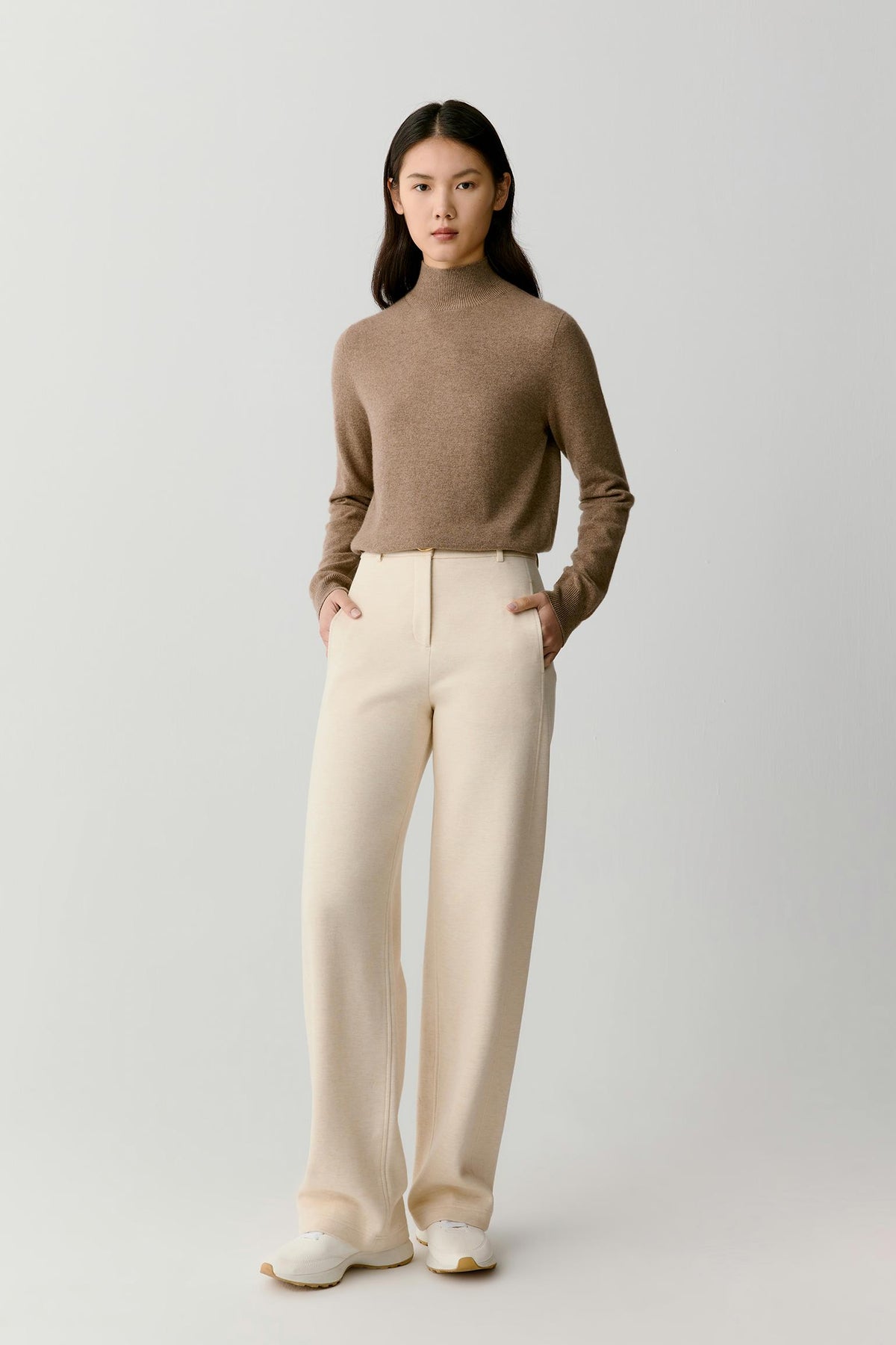 Full-length view of a woman wearing a taupe melange cashmere pullover, highlighting the relaxed fit and fine-knit construction.