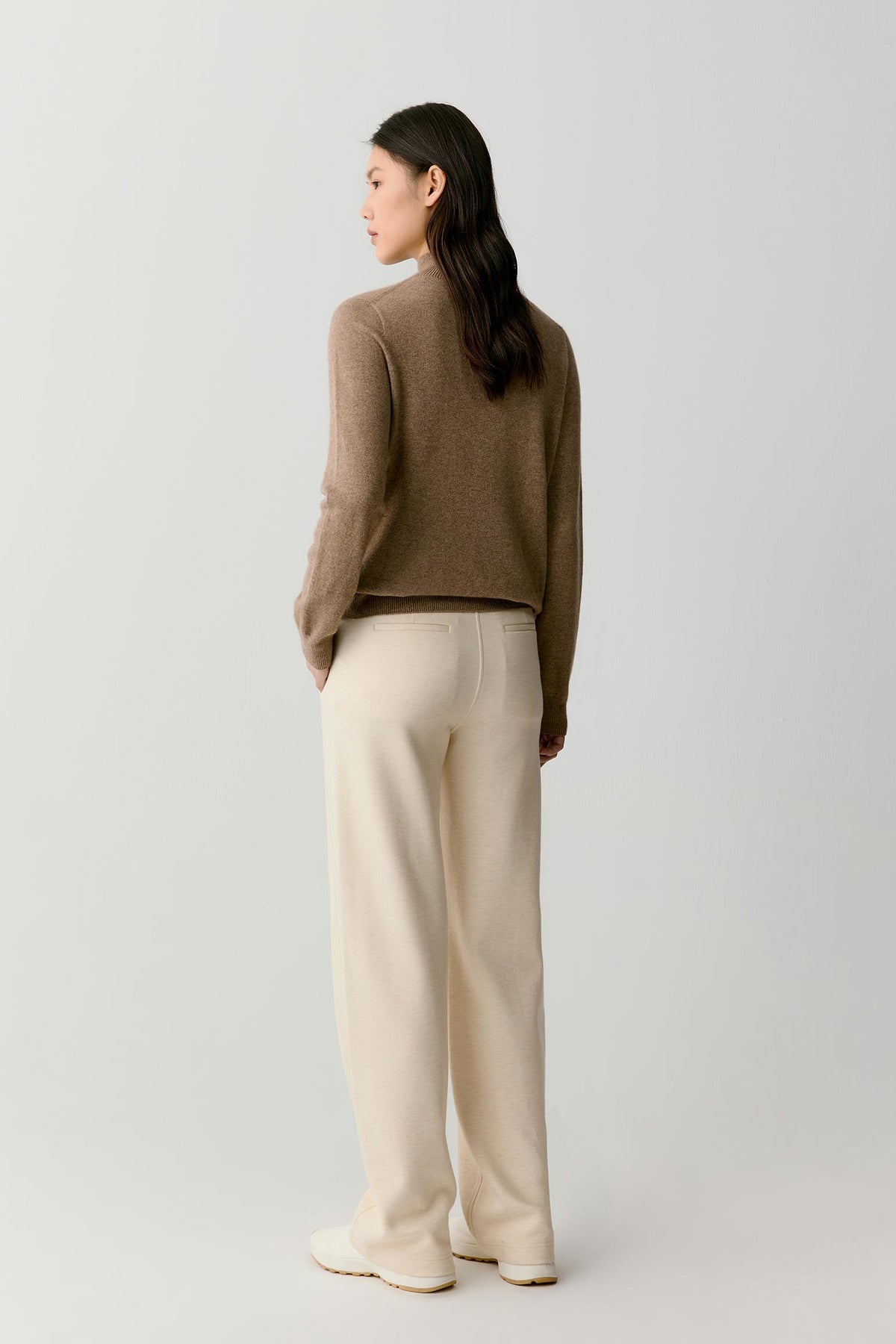 Back view of a woman wearing the taupe melange cashmere pullover, showing the mock neck, dropped shoulders and clean silhouette.