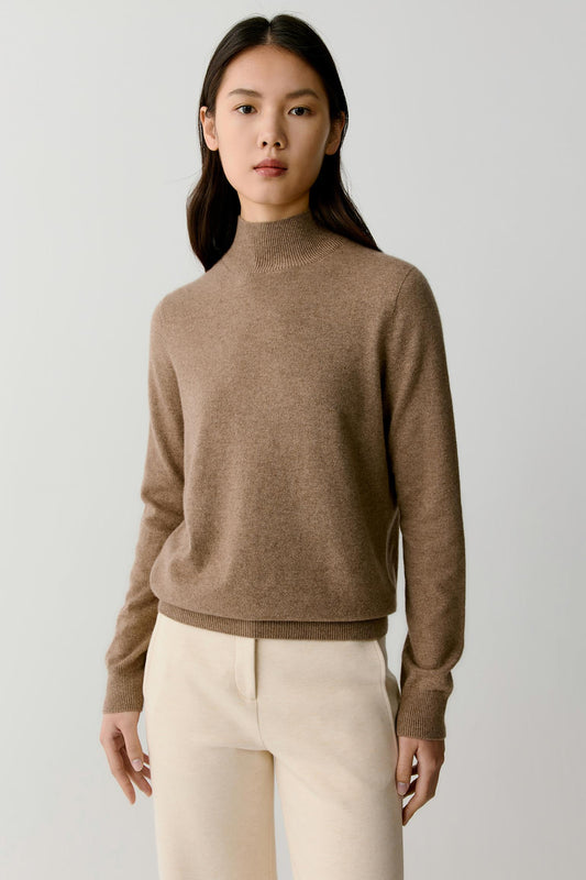 Front view of a woman wearing a taupe melange cashmere pullover, showing the mock neck, dropped shoulders and relaxed silhouette.