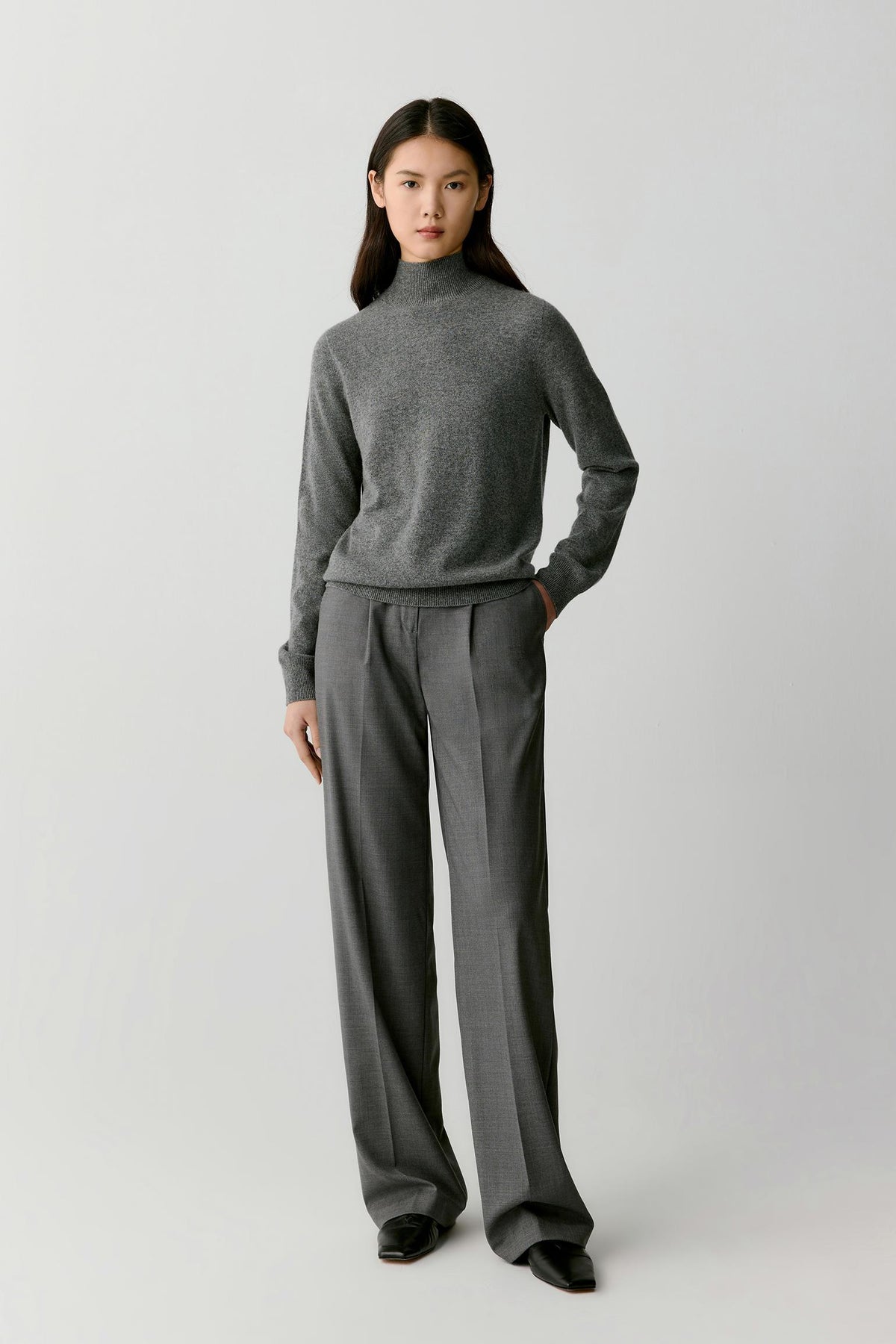 Full-length view of a woman wearing a smoky grey cashmere pullover, highlighting the relaxed fit and fine-knit construction.