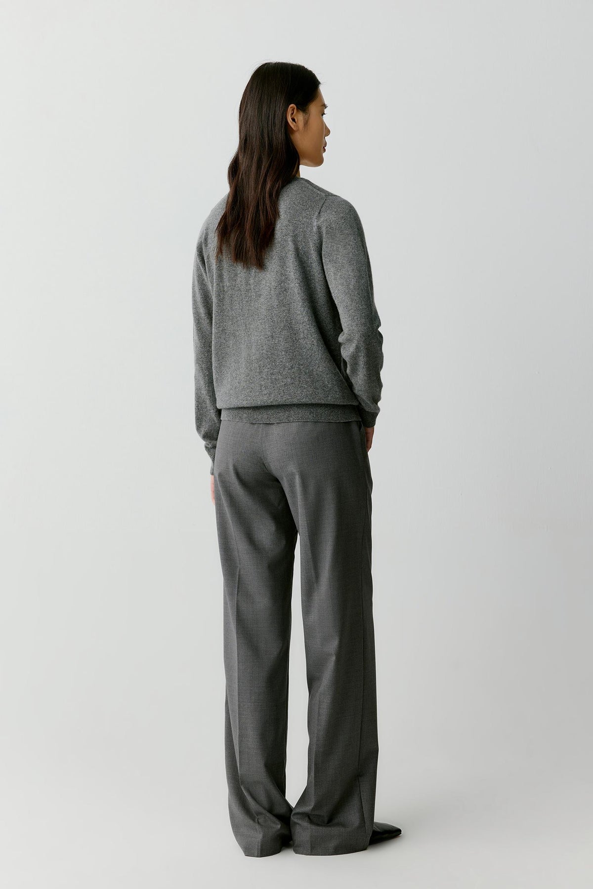 A woman shown from the back wearing a gray knit sweater and matching gray wide-leg trousers, standing against a plain light gray studio background.