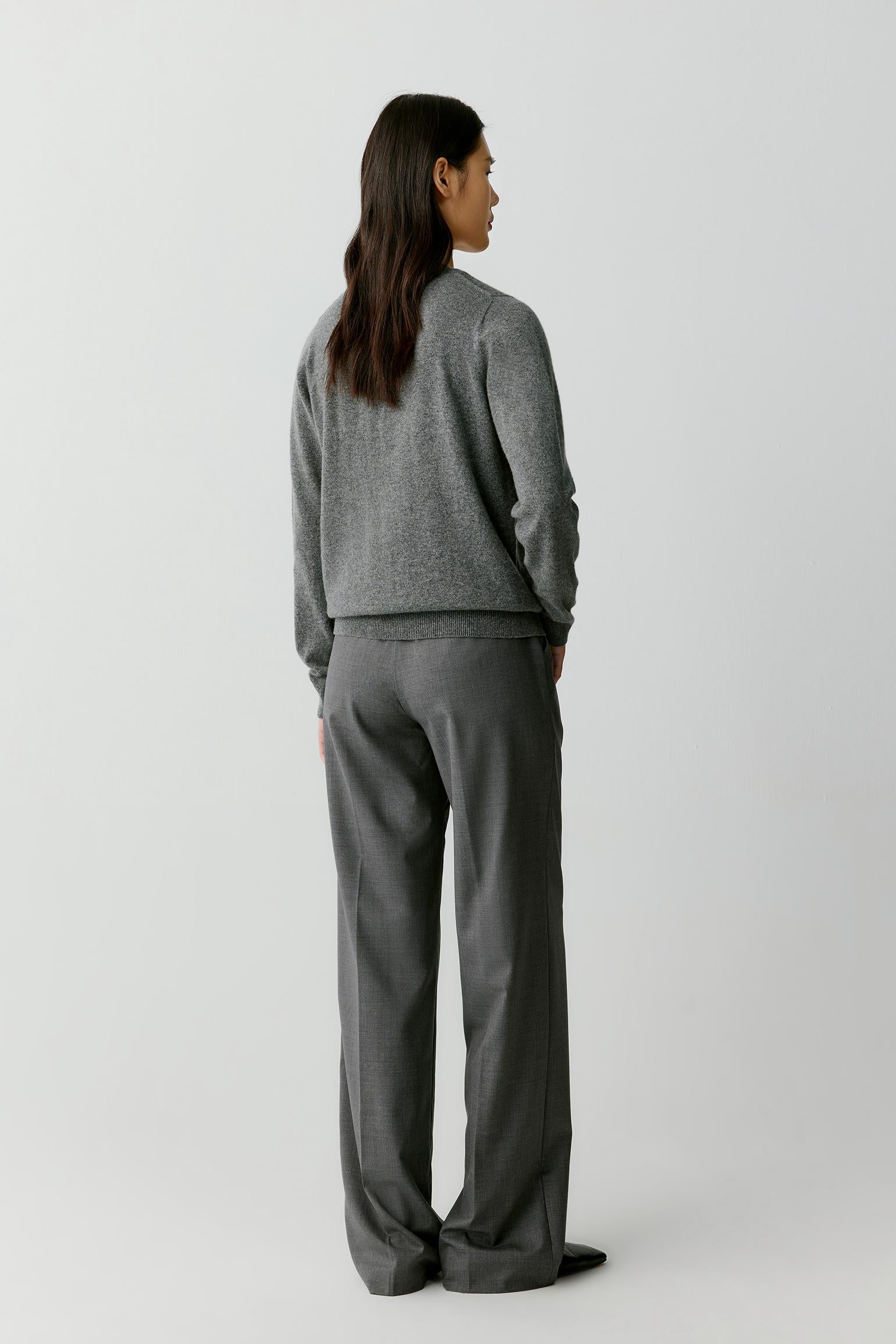 A woman shown from the back wearing a gray knit sweater and matching gray wide-leg trousers, standing against a plain light gray studio background.