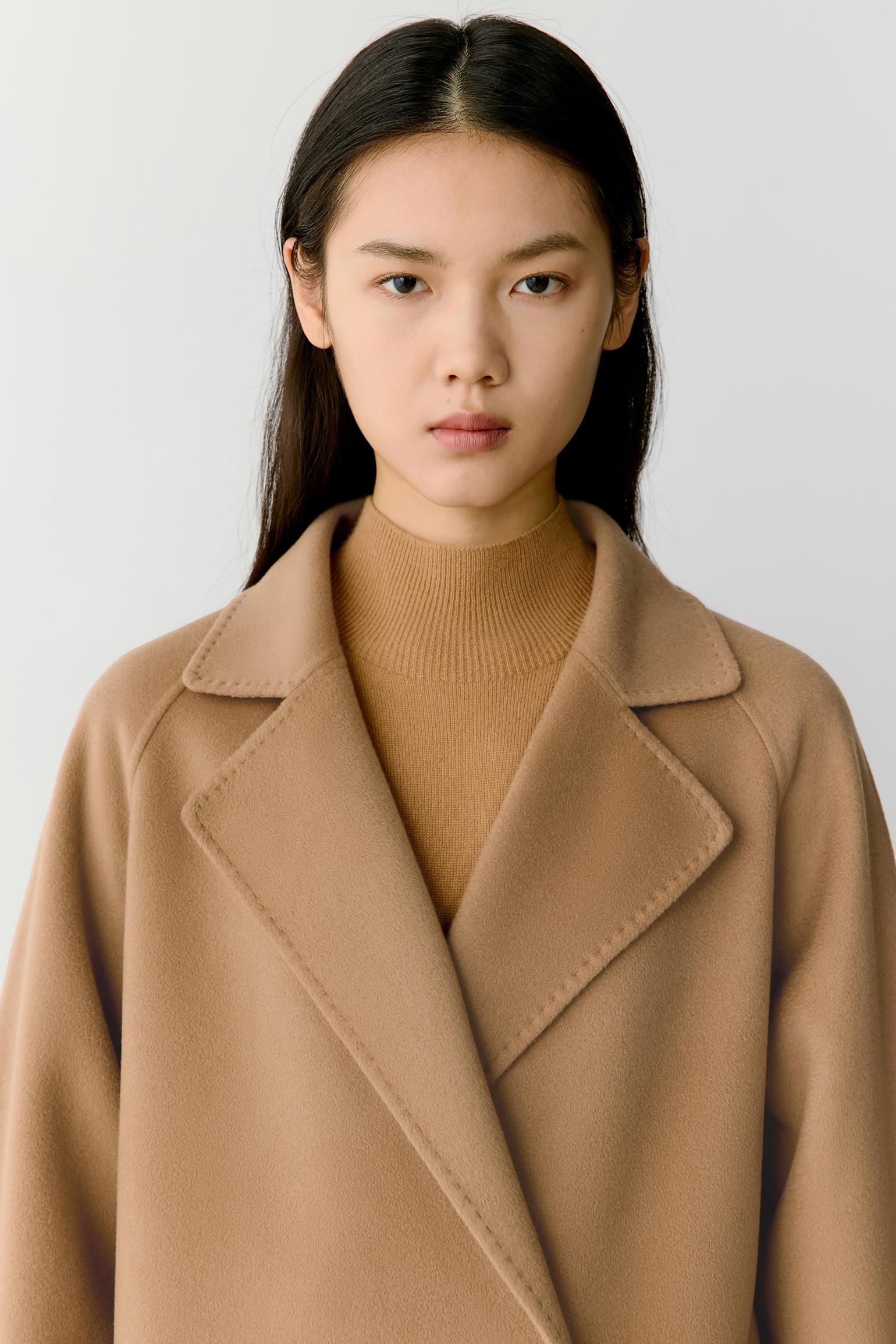 A model wearing a camel brown wool coat over a matching ribbed knit turtleneck sweater, photographed against a neutral light gray background.