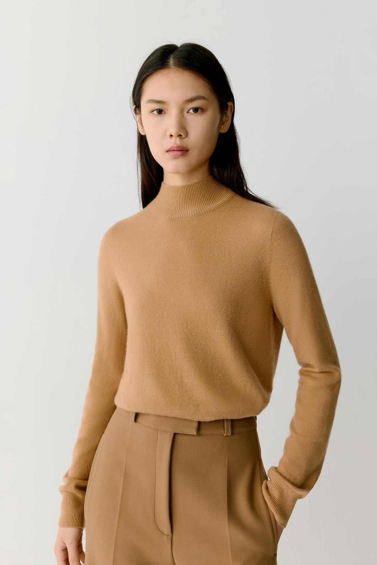 Three-quarter view highlighting the mock neck, long sleeves and fine-knit construction of the camel cashmere pullover.