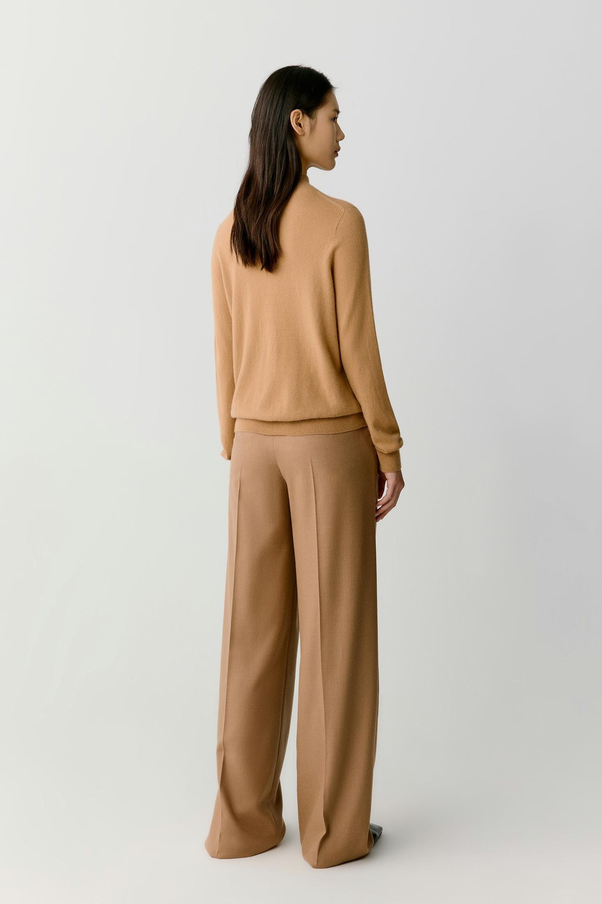 Side view of a woman wearing the camel cashmere pullover, showing the relaxed silhouette and clean knit construction.