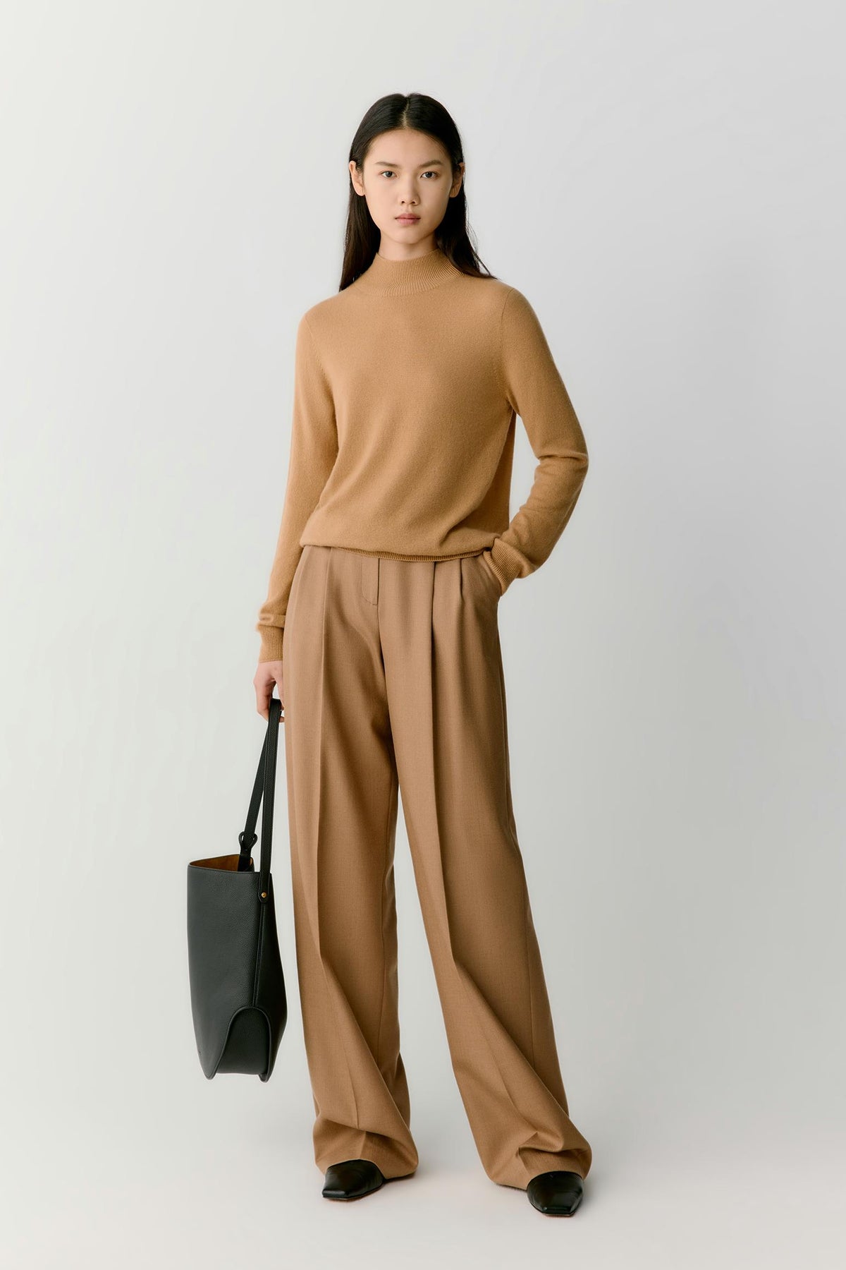 Front view of a woman wearing a camel cashmere pullover, showing the mock neck, dropped shoulders and relaxed silhouette.