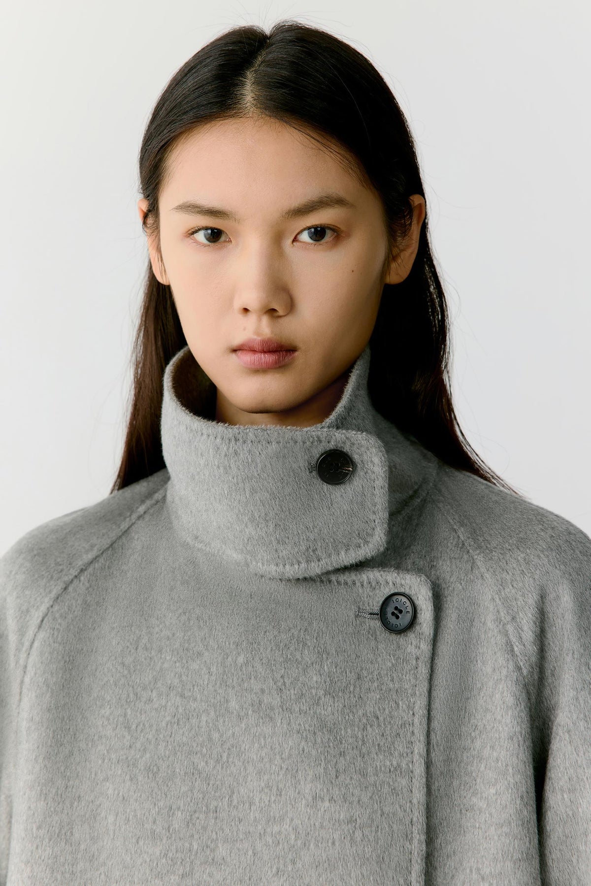 Close-up highlighting the high stand collar, asymmetric button fastening and soft grey melange cashmere surface.