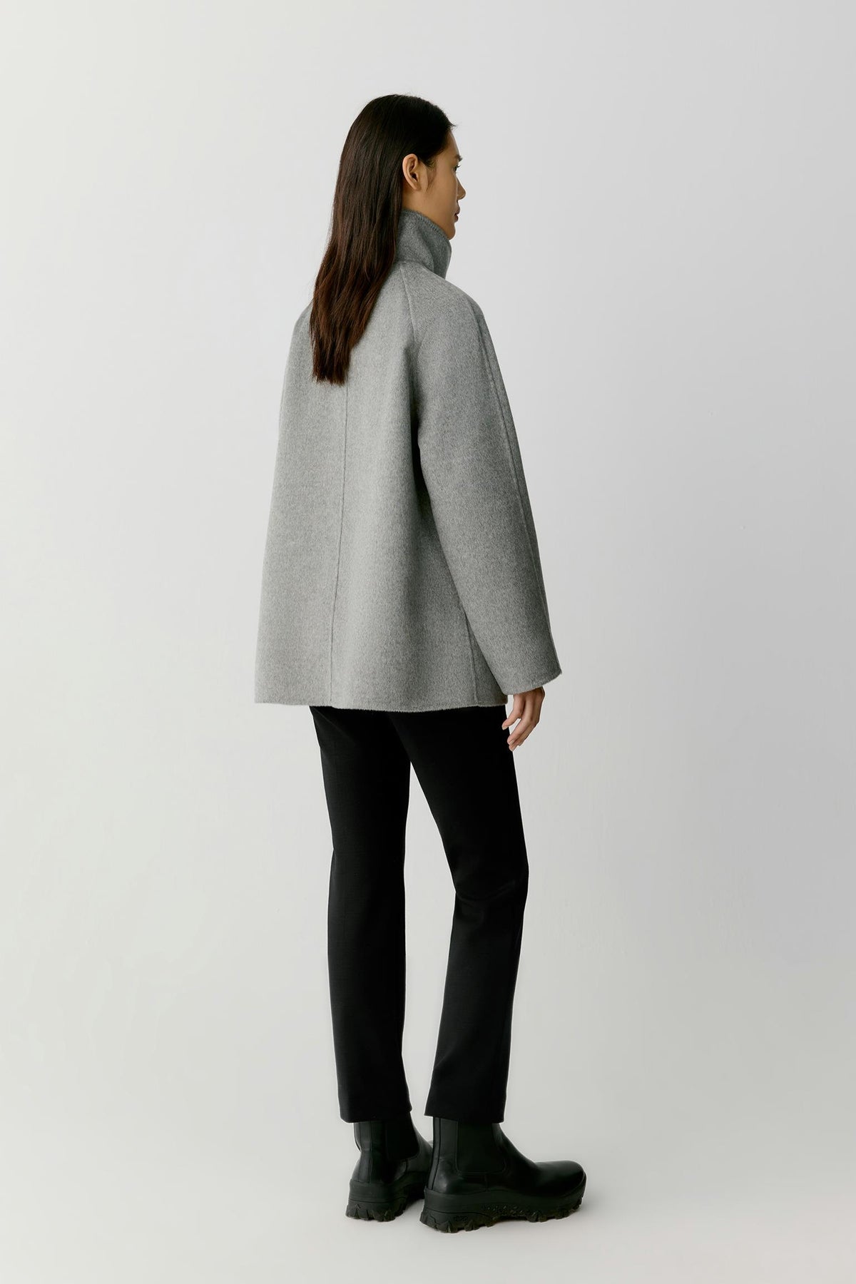 Back view of a woman wearing the grey melange double-face cashmere short coat, showing the relaxed silhouette and clean construction.