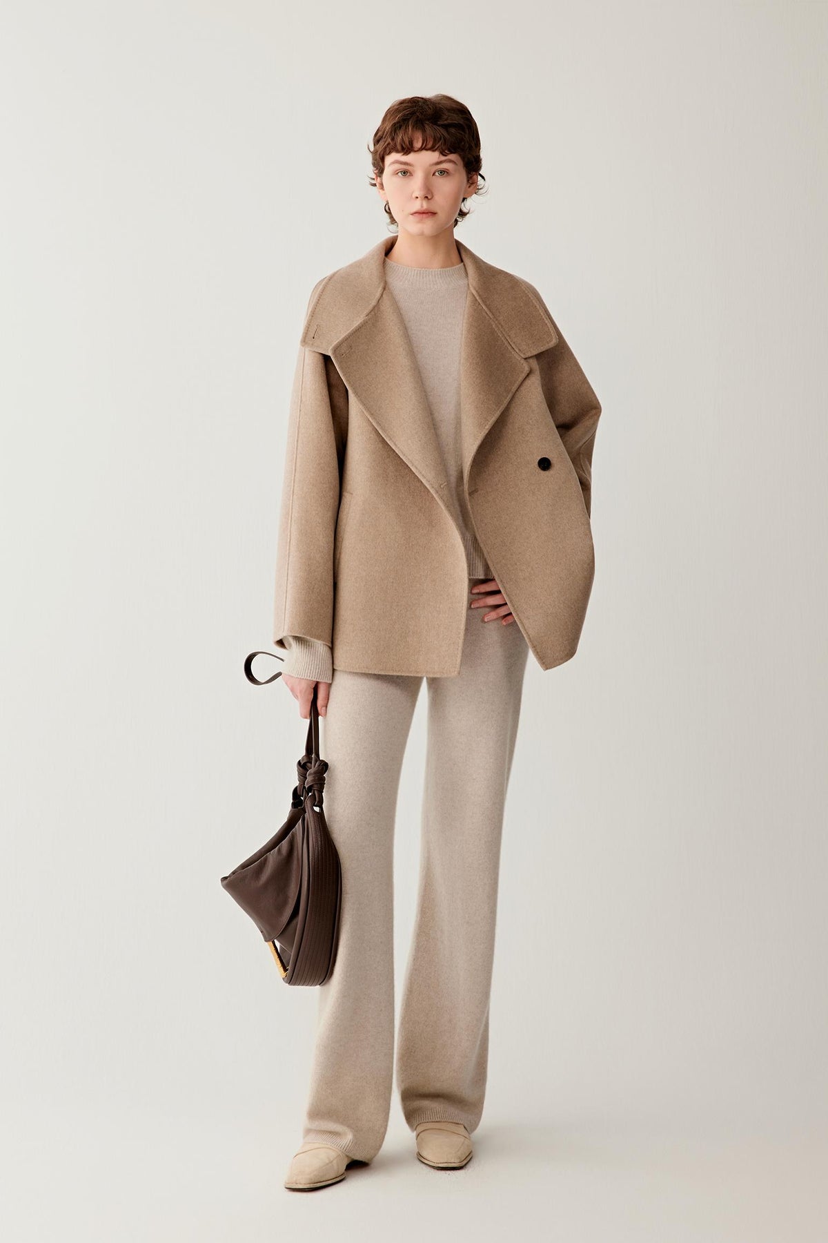 Front view of a woman wearing a natural beige double-face cashmere short coat, showing the high stand collar, asymmetric button fastening and relaxed silhouette.