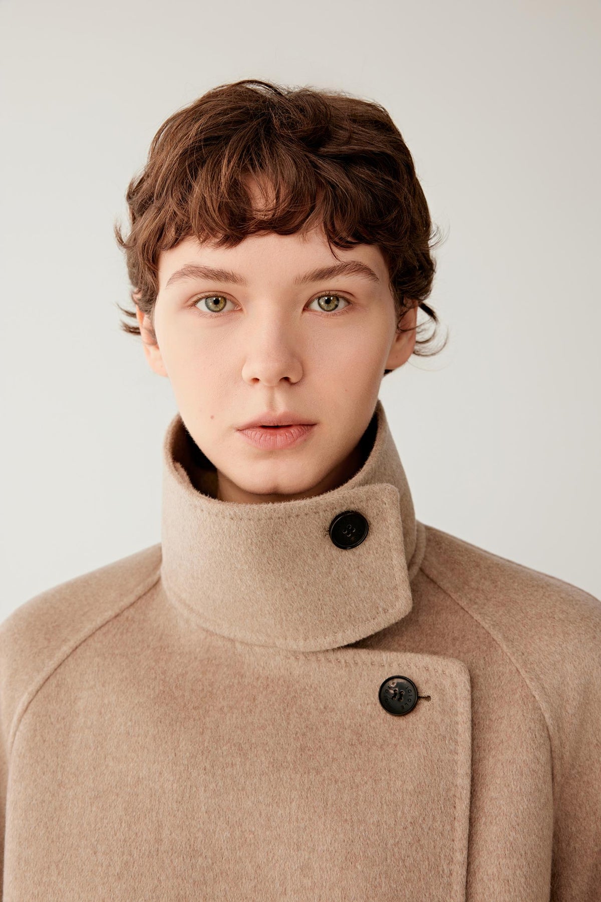 Close-up highlighting the high stand collar, asymmetric button fastening and soft natural beige cashmere surface.