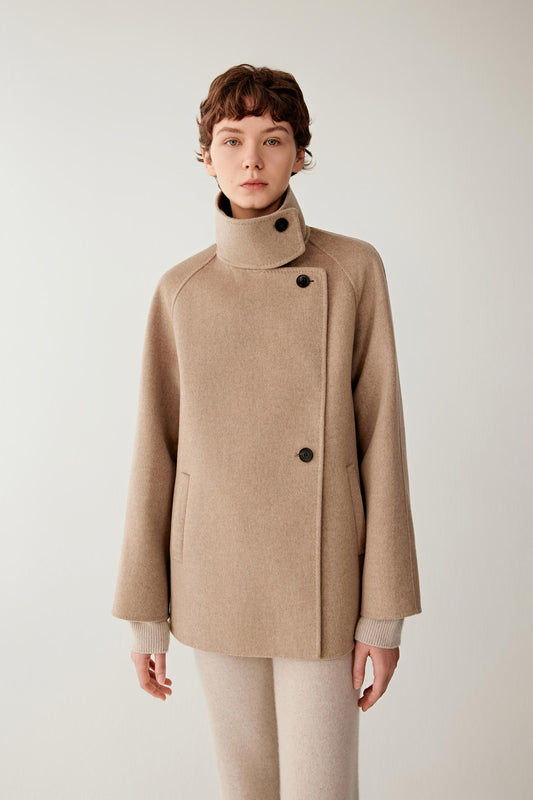 Three-quarter view highlighting the short cut, raglan sleeves and structured drape of the natural beige double-face cashmere coat.