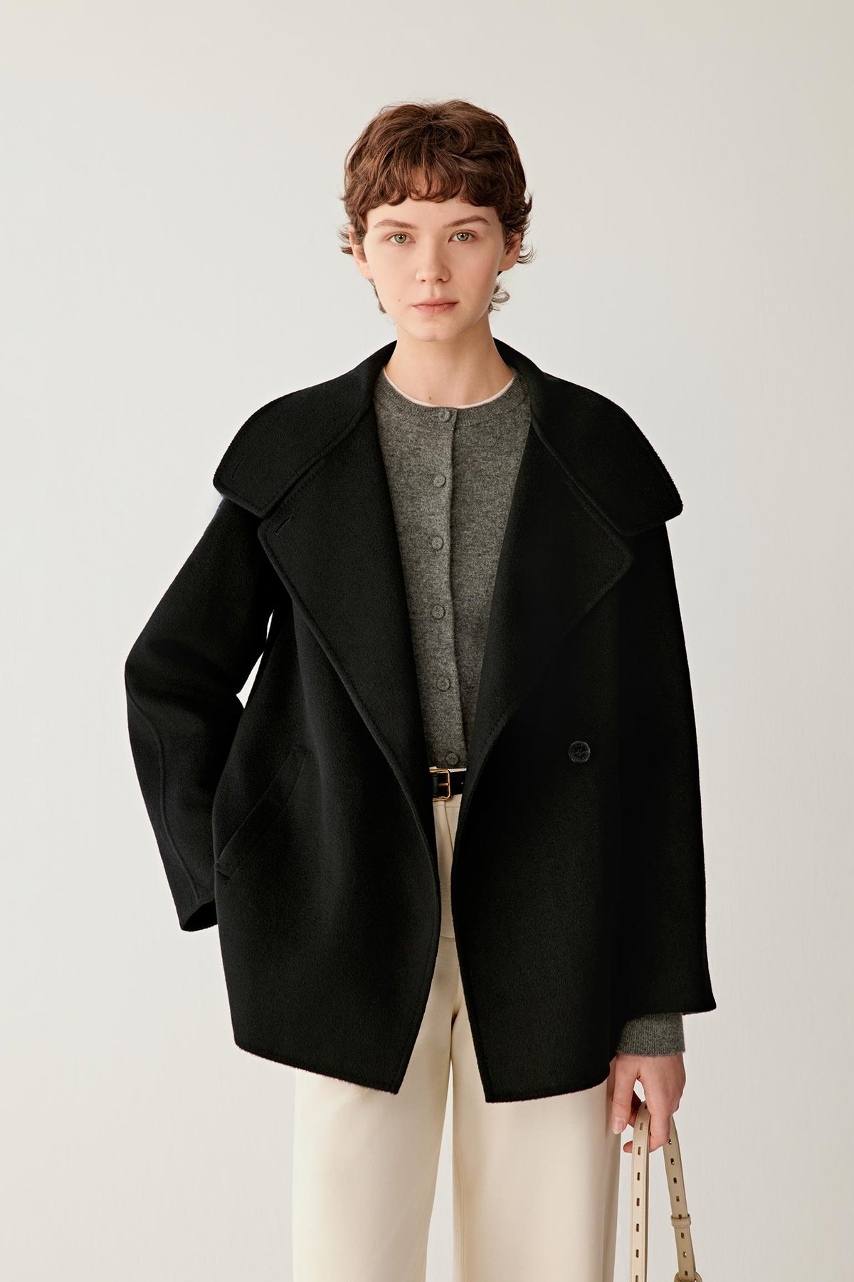 Three-quarter view highlighting the short cut, raglan sleeves and structured drape of the deep black double-face cashmere coat.