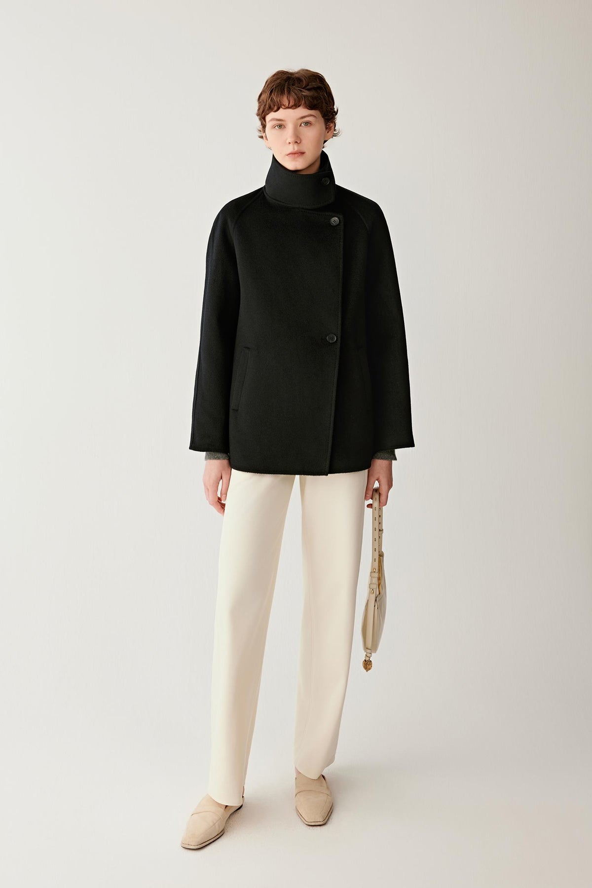 Front view of a woman wearing a deep black double-face cashmere short coat, showing the high stand collar, asymmetric button fastening and relaxed silhouette.
