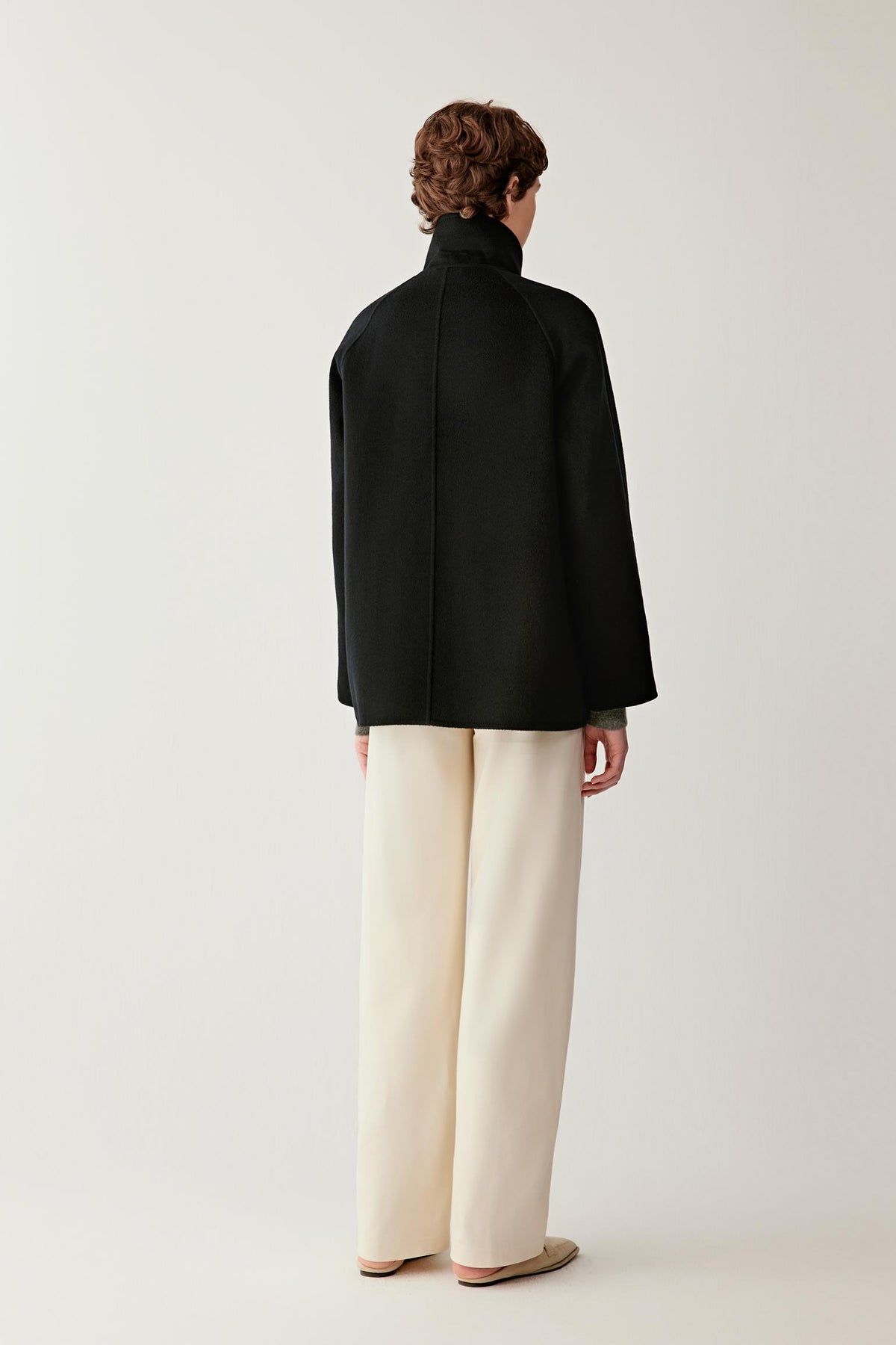 Back view of a woman wearing the deep black double-face cashmere short coat, showing the relaxed silhouette and clean construction.