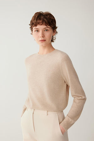 Front view of a woman wearing a light beige cashmere pullover, showing the crew neckline, long sleeves and relaxed silhouette.