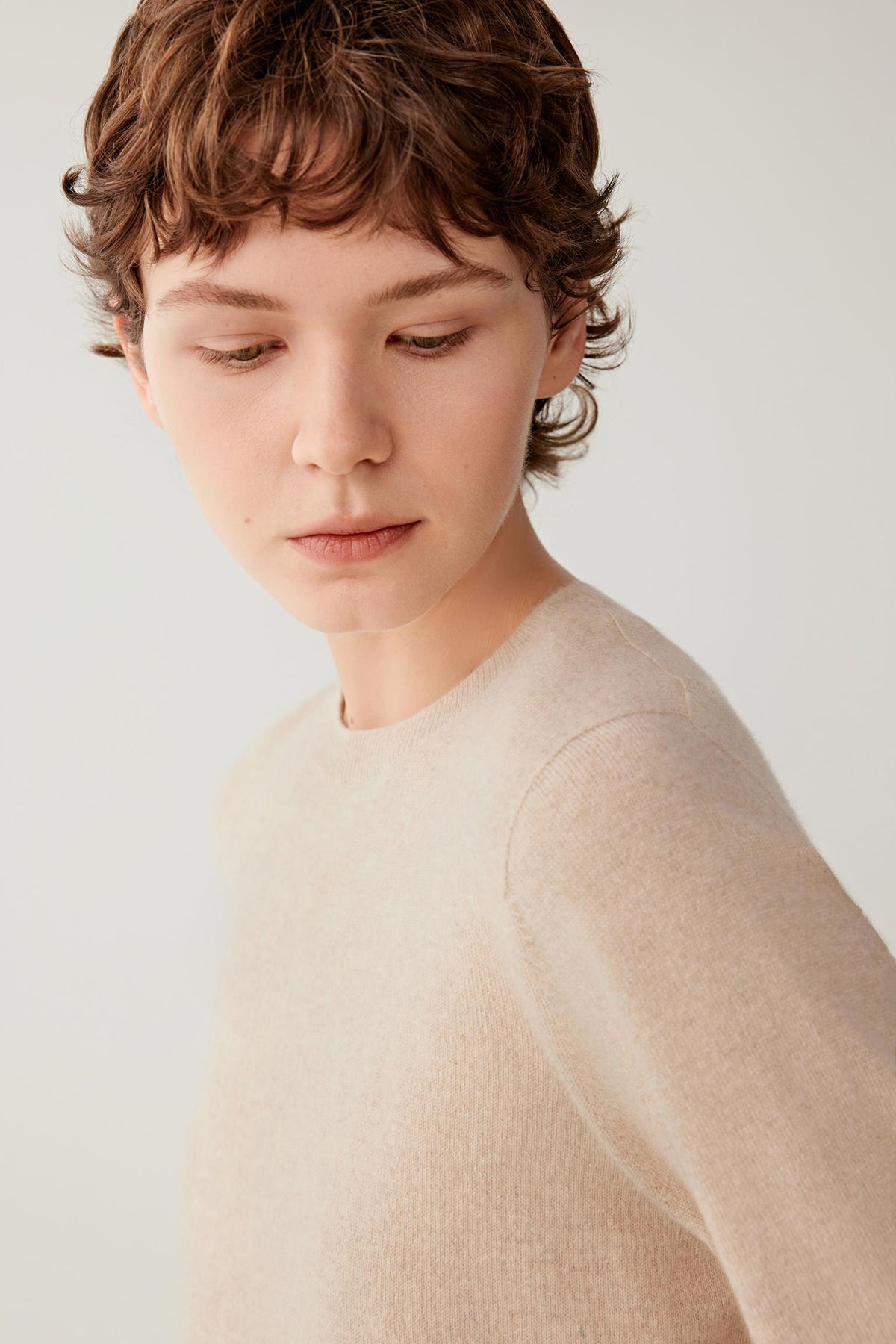 Close-up highlighting the crew neckline and fine-knit texture of the light beige cashmere pullover.