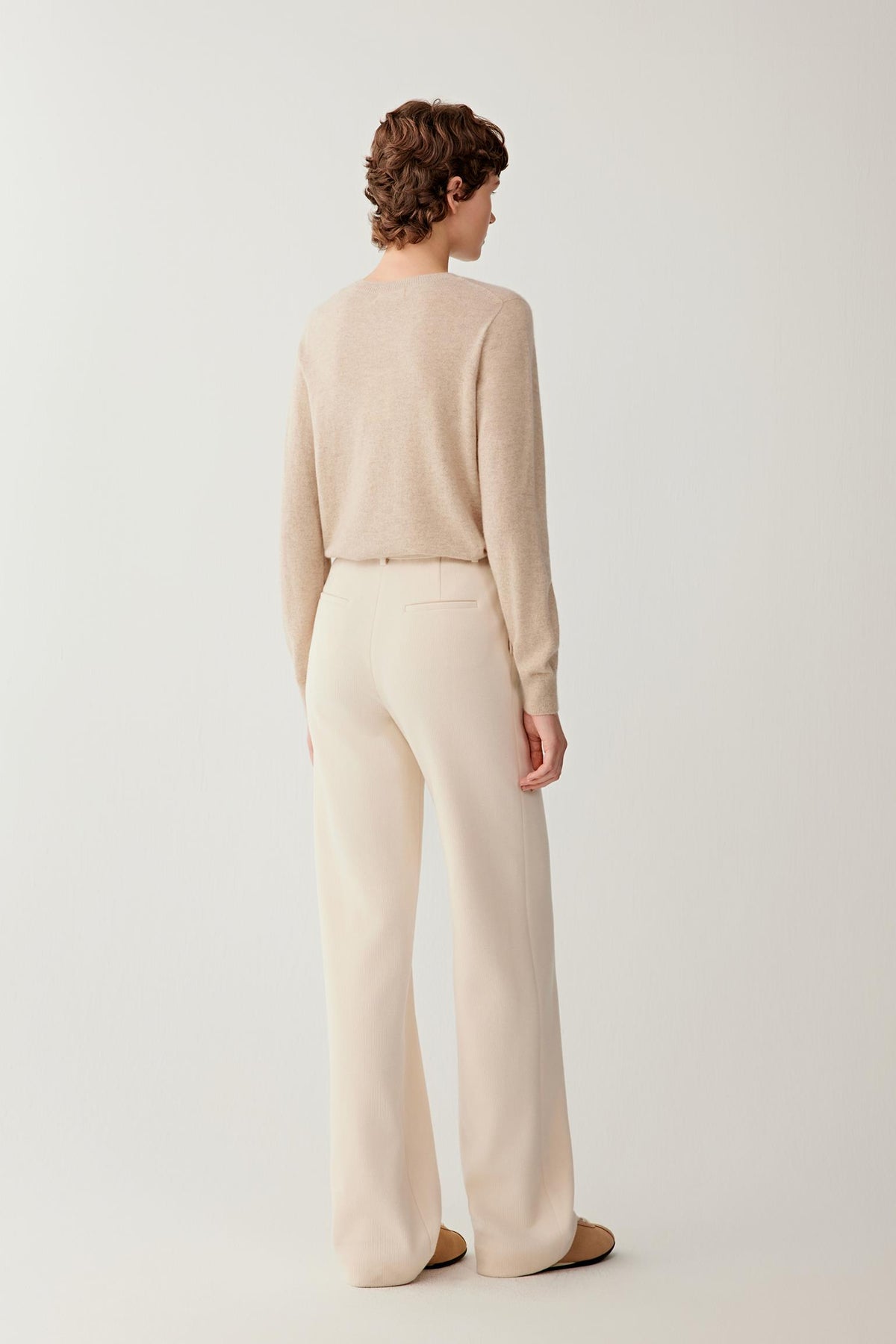 Back view of a woman wearing the light beige cashmere pullover, showing the clean silhouette and long sleeves.
