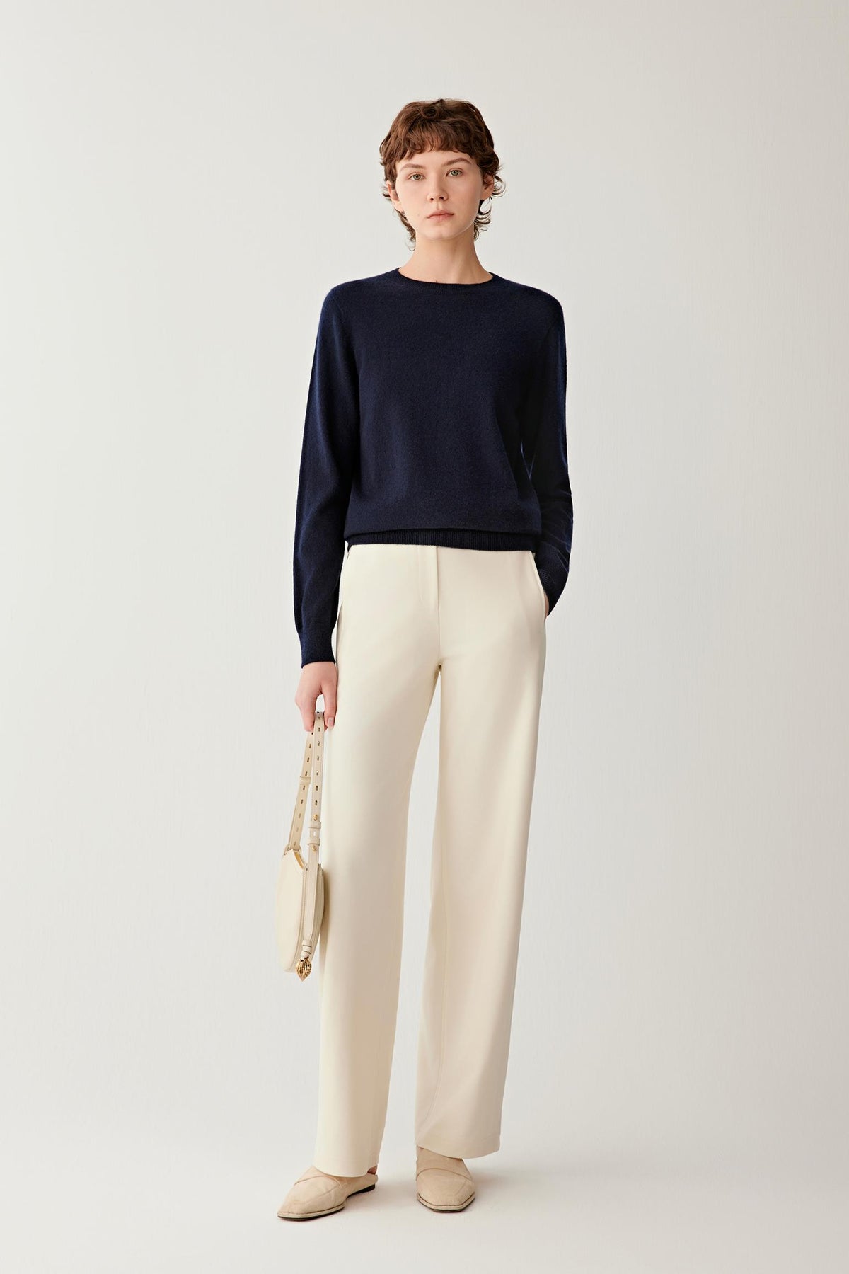 Full-length front view of women’s navy cashmere pullover styled with white trousers