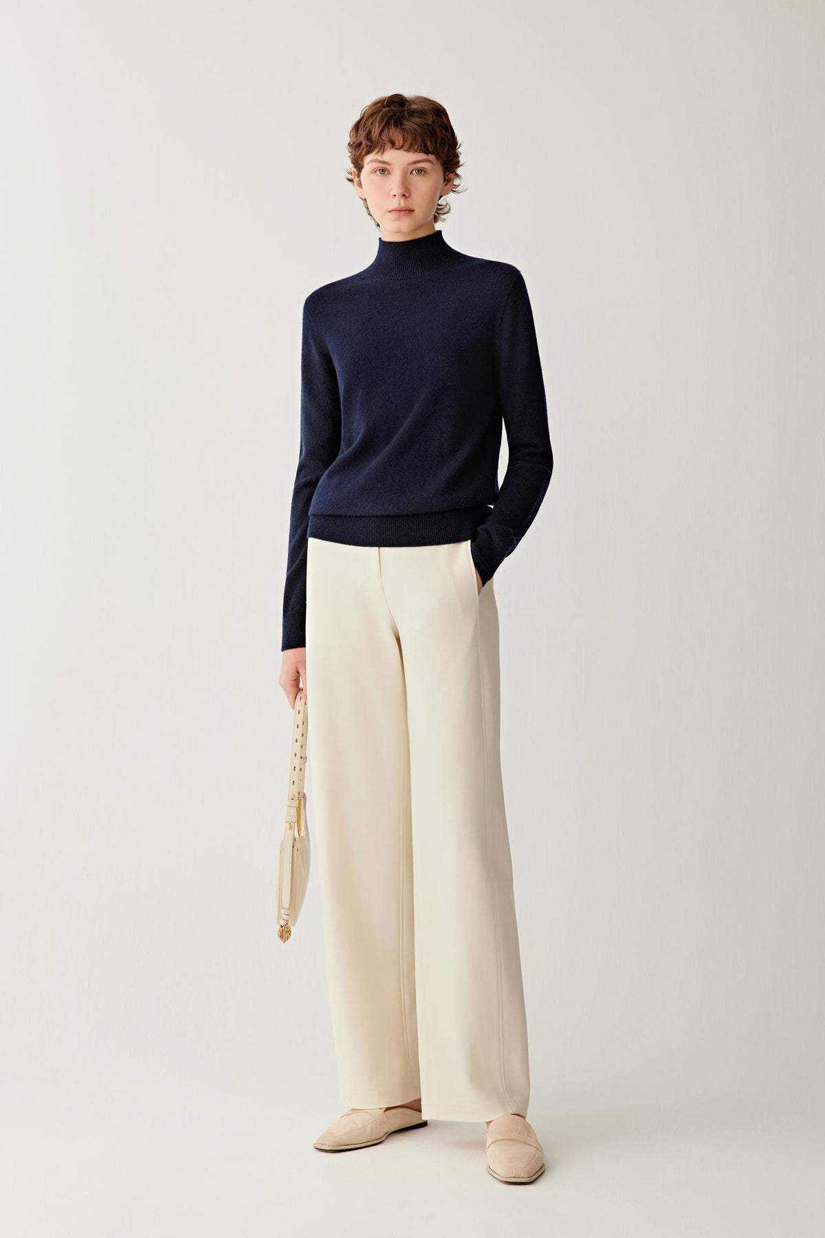 Front view of a woman wearing a navy cashmere pullover, showing the mock neck, dropped shoulders and relaxed silhouette.