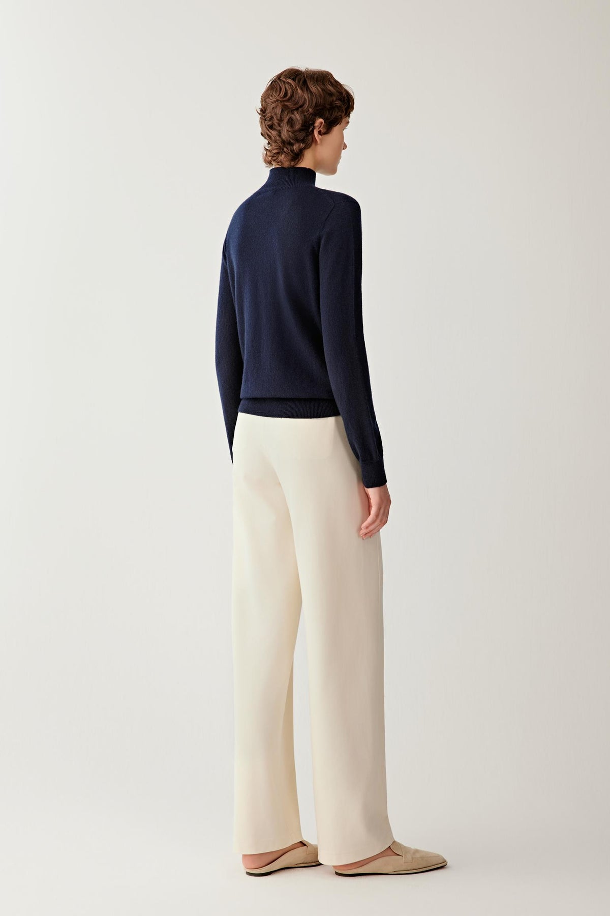 Back view of a woman wearing the navy cashmere pullover, showing the clean silhouette and fine-knit construction.