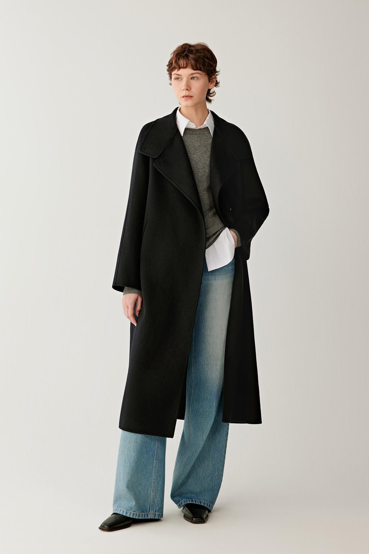 Front view of a woman wearing a deep black double-face cashmere long coat, showing the high stand collar, asymmetric button fastening and long silhouette.