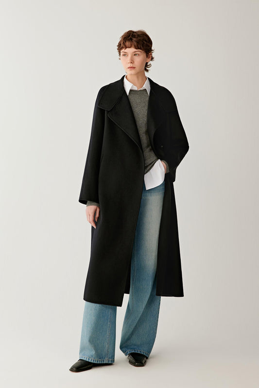 Front view of a woman wearing a deep black double-face cashmere long coat, showing the high stand collar, asymmetric button fastening and long silhouette.