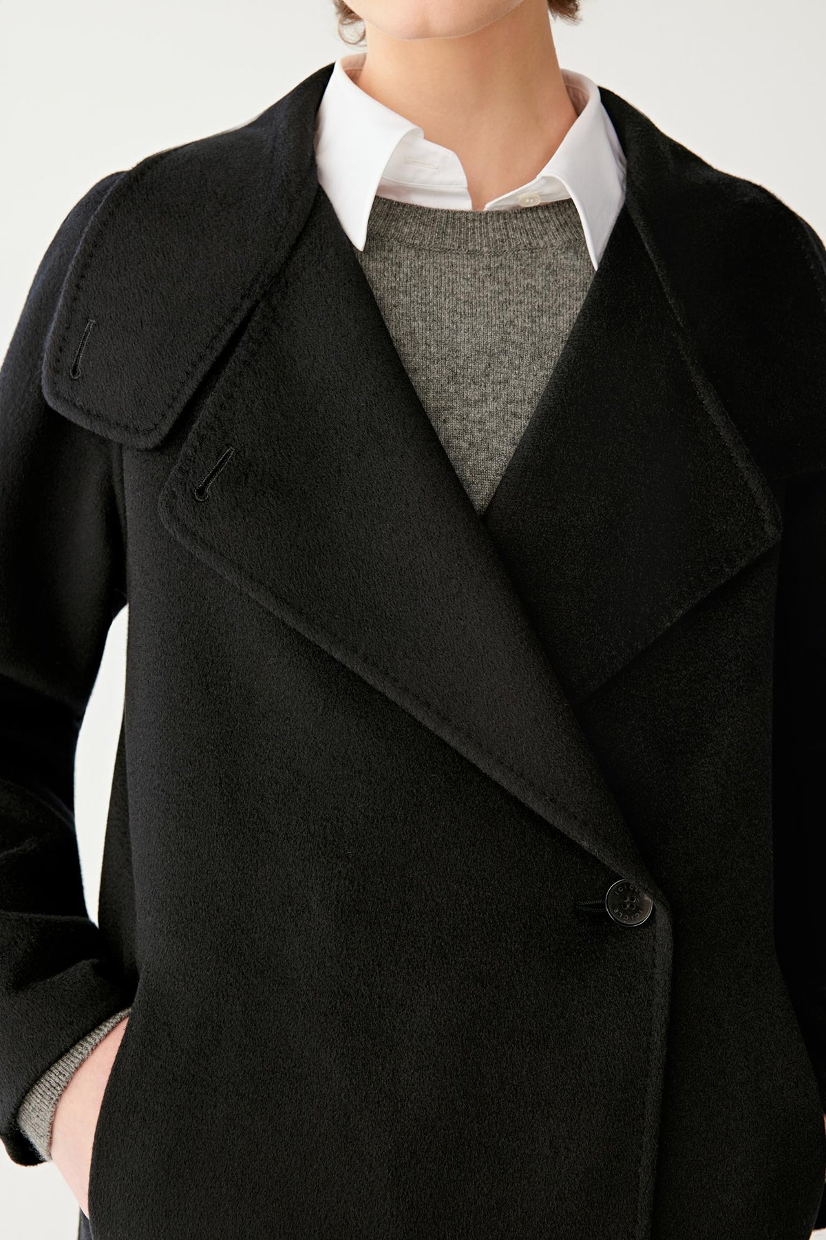 Close-up highlighting the asymmetric front construction, button fastening and dense black double-face cashmere surface.