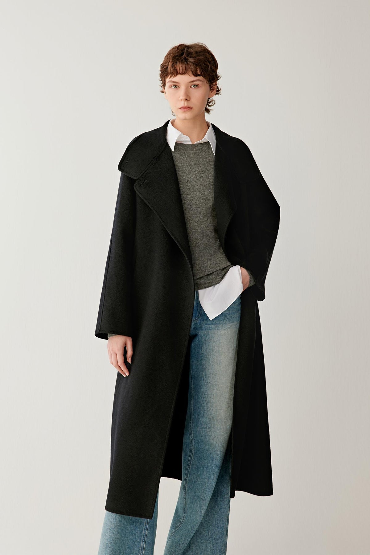 Three-quarter view highlighting the long cut, asymmetric front fastening and structured drape of the deep black double-face cashmere coat.