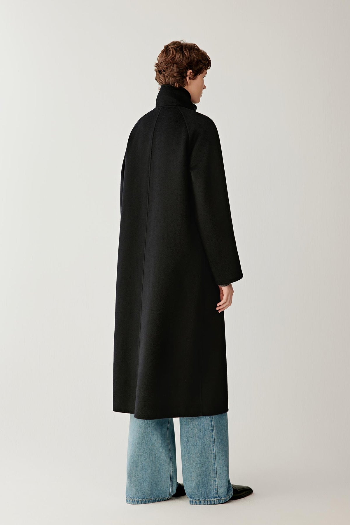 Back view of a woman wearing the deep black double-face cashmere coat, showing the long silhouette, raglan sleeves and clean construction.