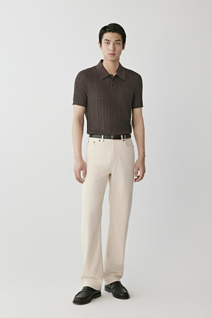Man wearing a brown knitted polo shirt with cream trousers and black loafers.