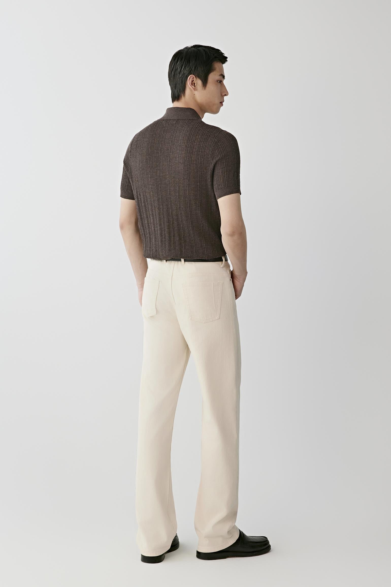 Man wearing a brown knitted polo shirt with cream trousers and black loafers.