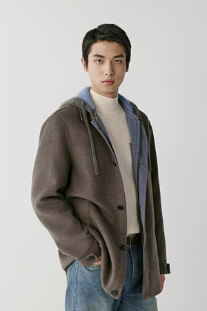 Front view of a man wearing a dark brown melange merino wool coat, showing the hood, front button fastening and welt pockets.
