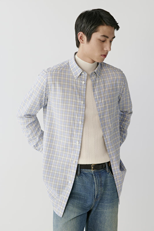 Front view of a man wearing a light blue, grey and white checked worsted wool shirt, showing the classic collar, button-front fastening and straight hem.