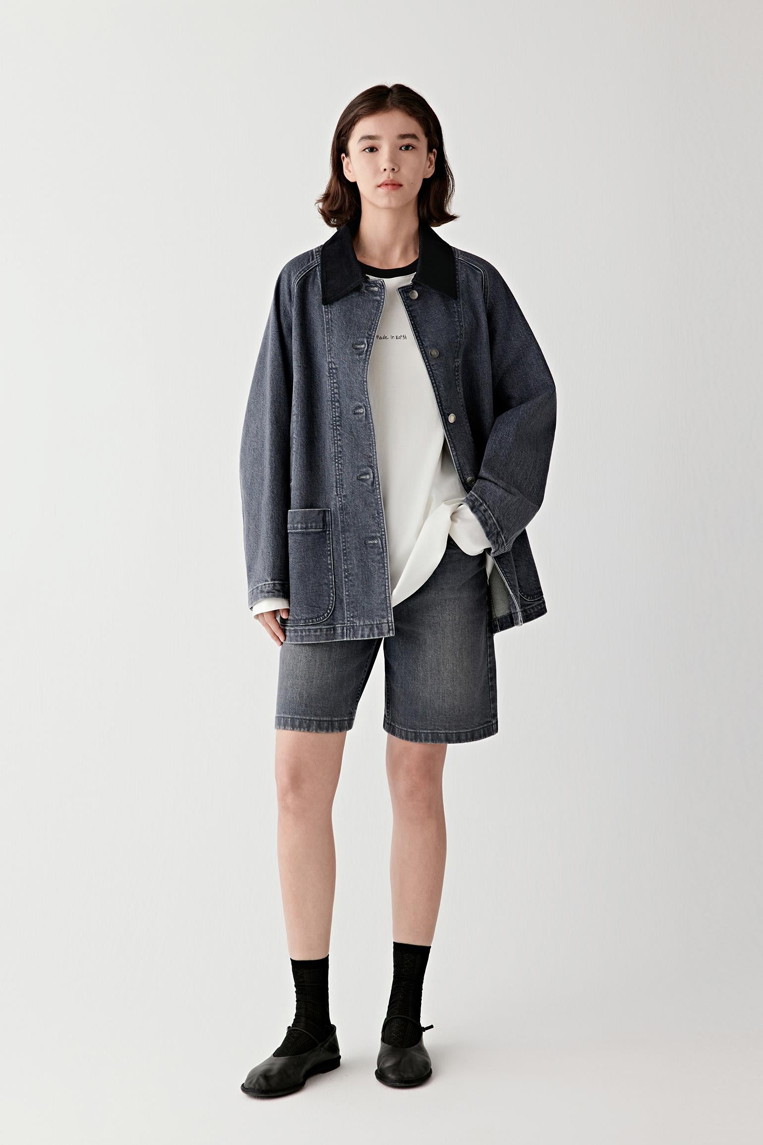 Full-length front view of a female model wearing a smoke grey stretch denim jacket with matching shorts, showing rounded patch pockets and relaxed fit.