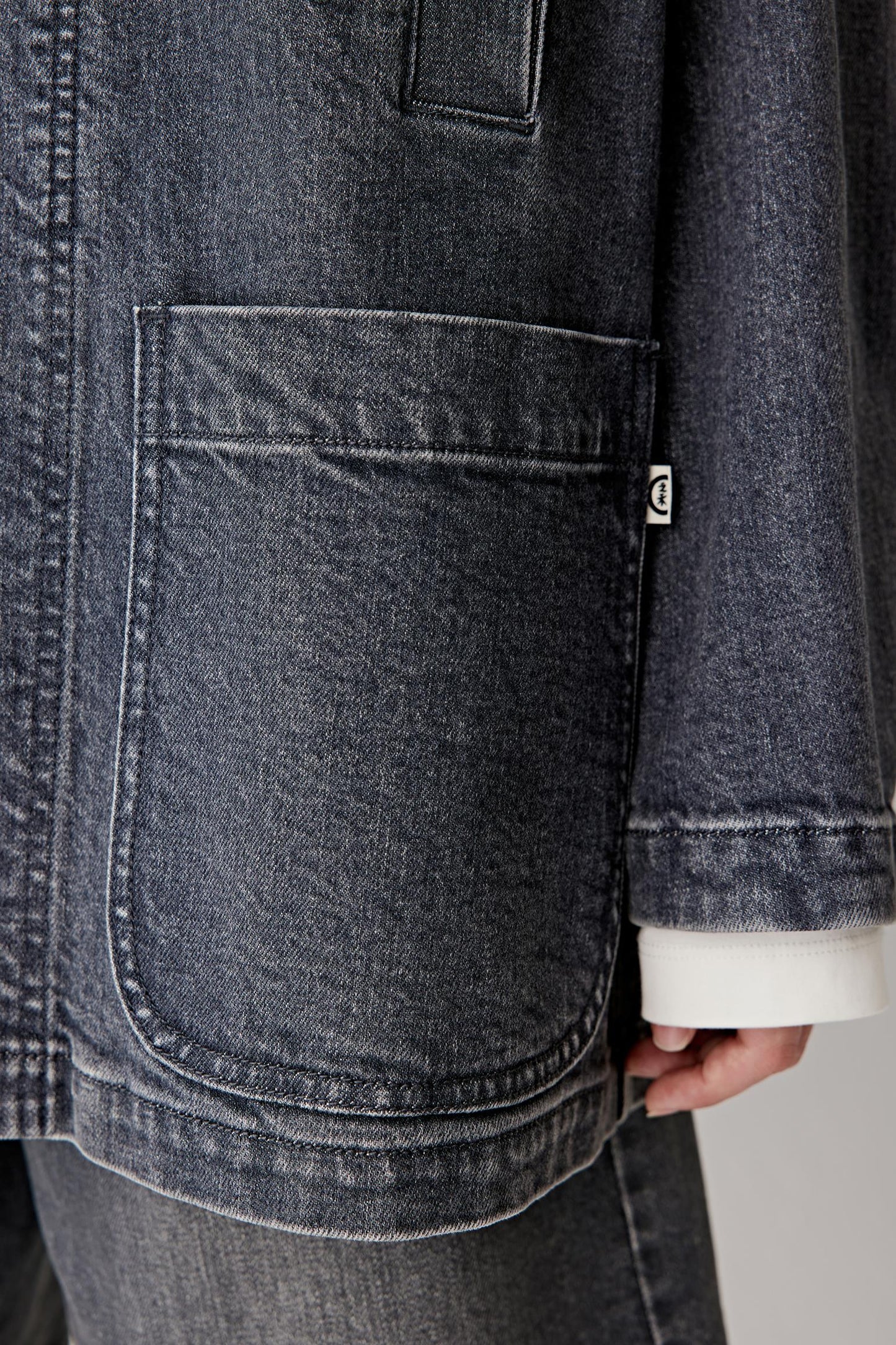 Detail of denim texture and pocket stitching, highlighting utilitarian finishing.