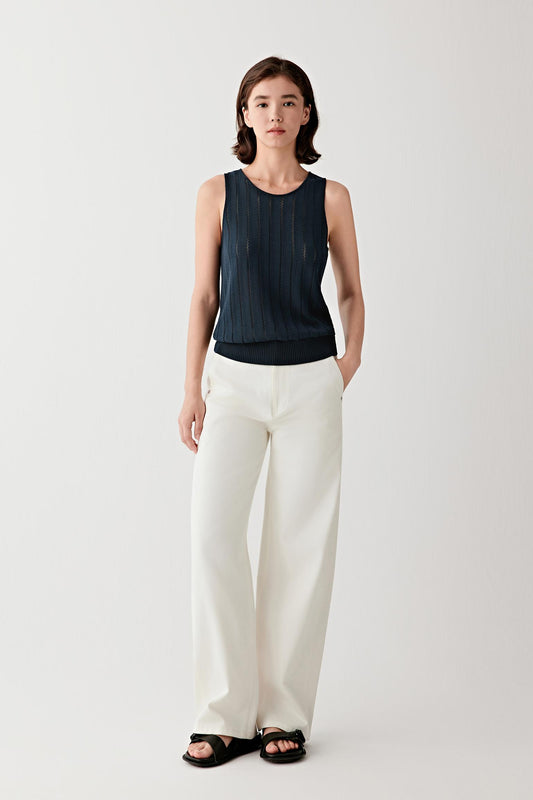 Full-length front view of a woman standing facing forward wearing undyed earth-tone denim straight-leg trousers in a light ecru shade, paired with a dark sleeveless knit top, highlighting the clean straight silhouette, structured yet soft hand of the denim and the natural color contrast