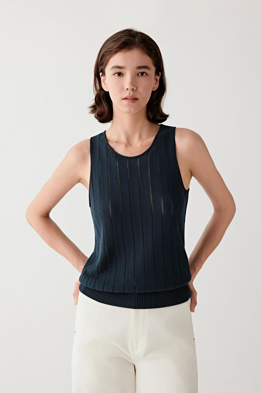 Front view portrait of a woman wearing a navy silk and cotton knit sleeveless top, paired with light ivory trousers, highlighting the fitted silhouette, clean armholes and the vertical openwork knit structure with a subtly textured surface