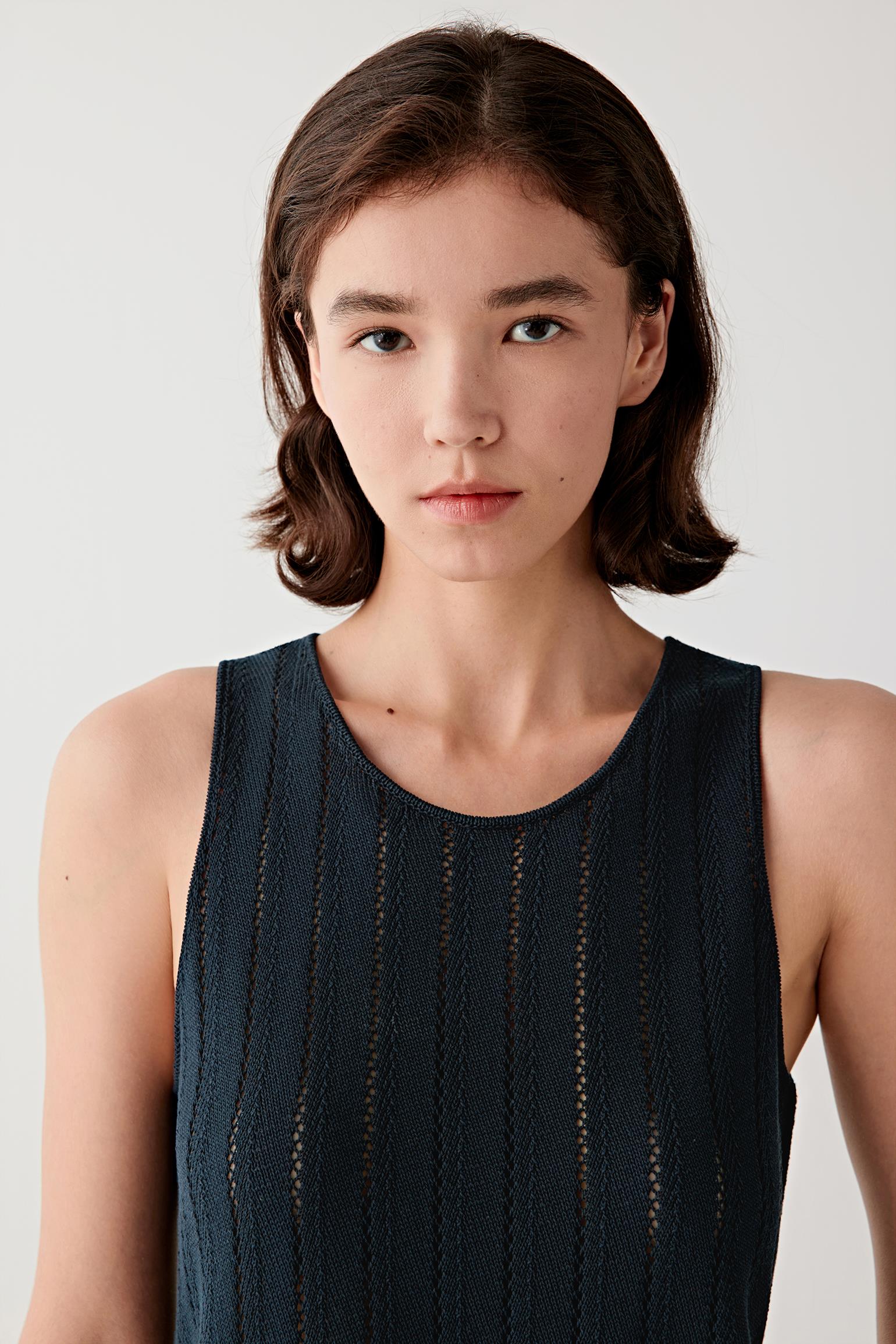 Close-up portrait of the upper body focusing on the neckline and shoulder line, showing the sleeveless cut, fine knit structure and the slightly sheer, breathable quality of the openwork vertical pattern