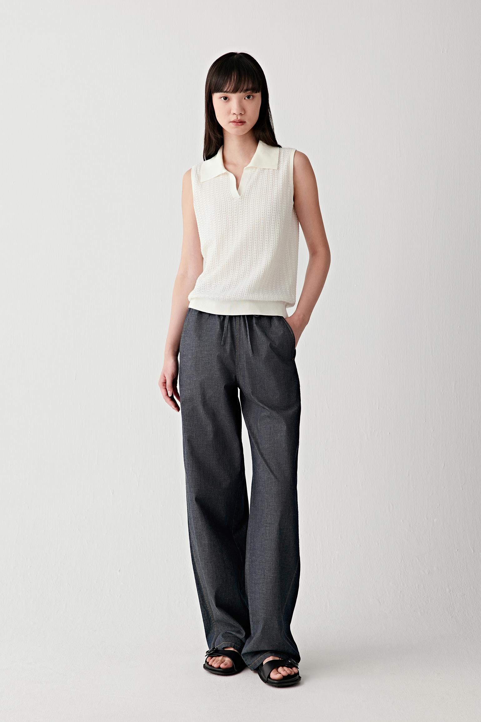 Full-length front view of a woman standing facing forward wearing navy denim wide-leg trousers with a relaxed fit, paired with a sleeveless white top, highlighting the fluid fall of the legs, the soft structure of the fabric and the elasticated waistband that sits naturally at the waist