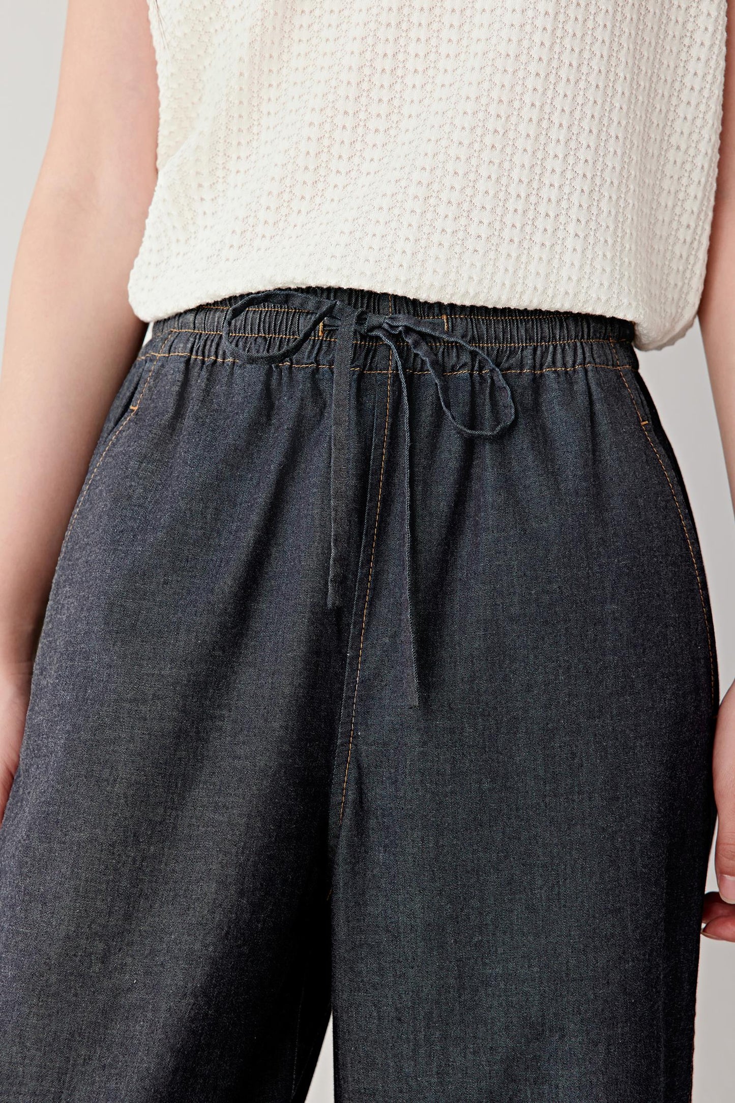 Close-up of the waistband and upper hip area, focusing on the elasticated waistband with drawstring detail, stitched eyelets and the gathered fabric creating subtle volume at the waist