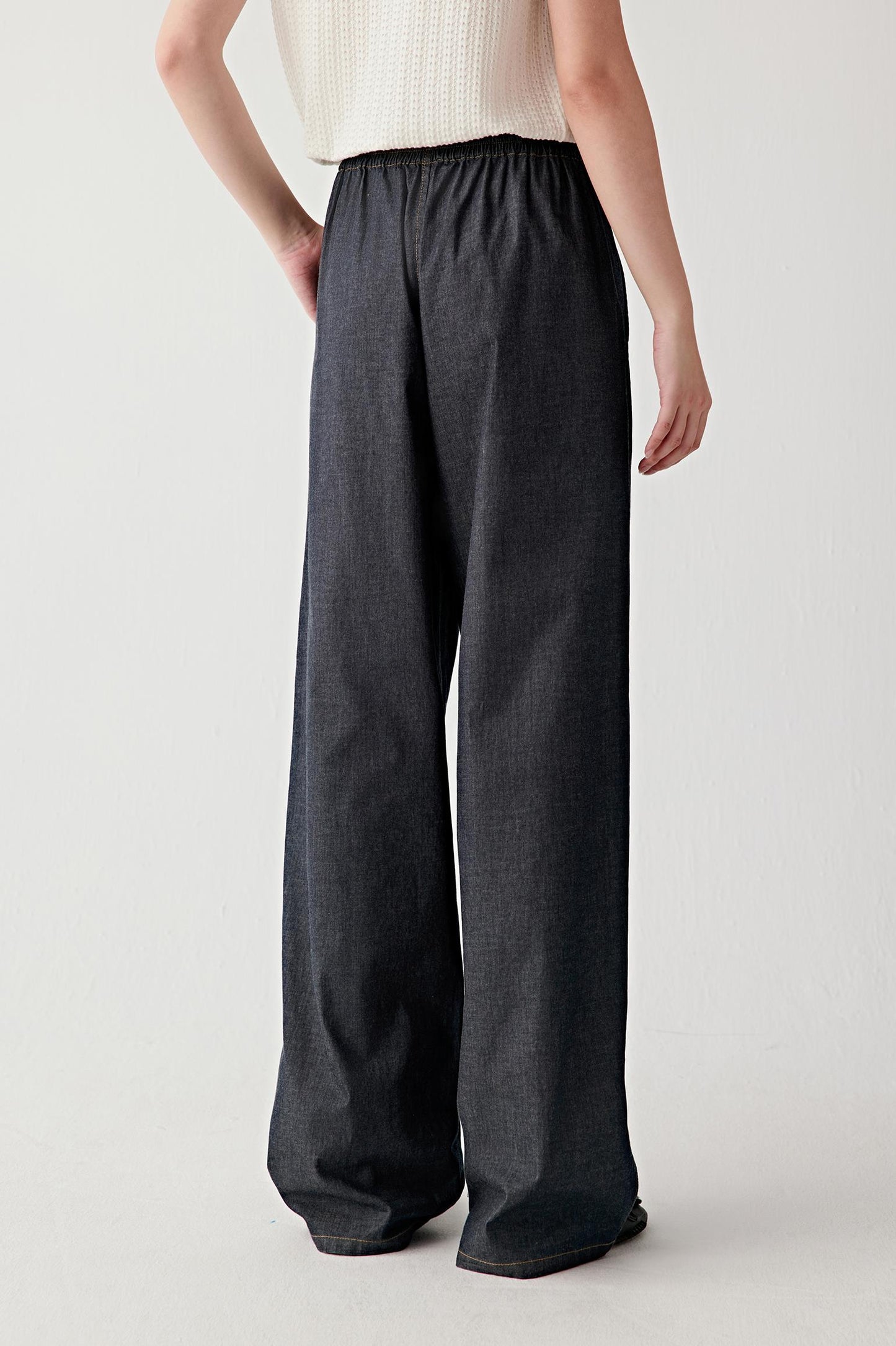 Side view showing the profile of the trousers, highlighting the volume through the leg, the straight outer seam line and the way the fabric moves with a soft, flexible drape