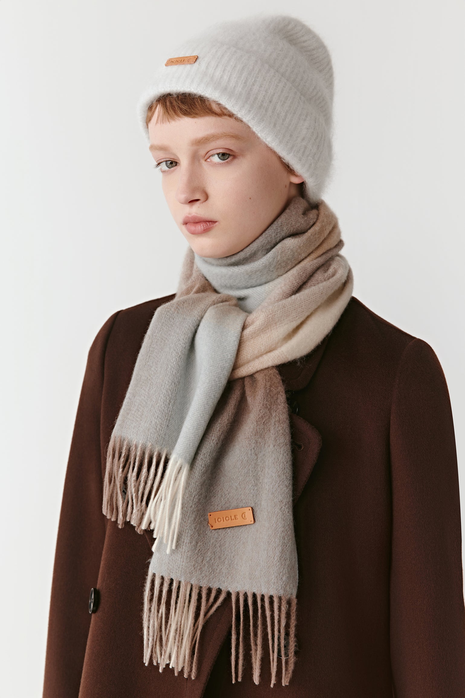 A woman wearing a beige and light-blue gradient cashmere scarf, paired with a soft knitted beanie and brown coat.