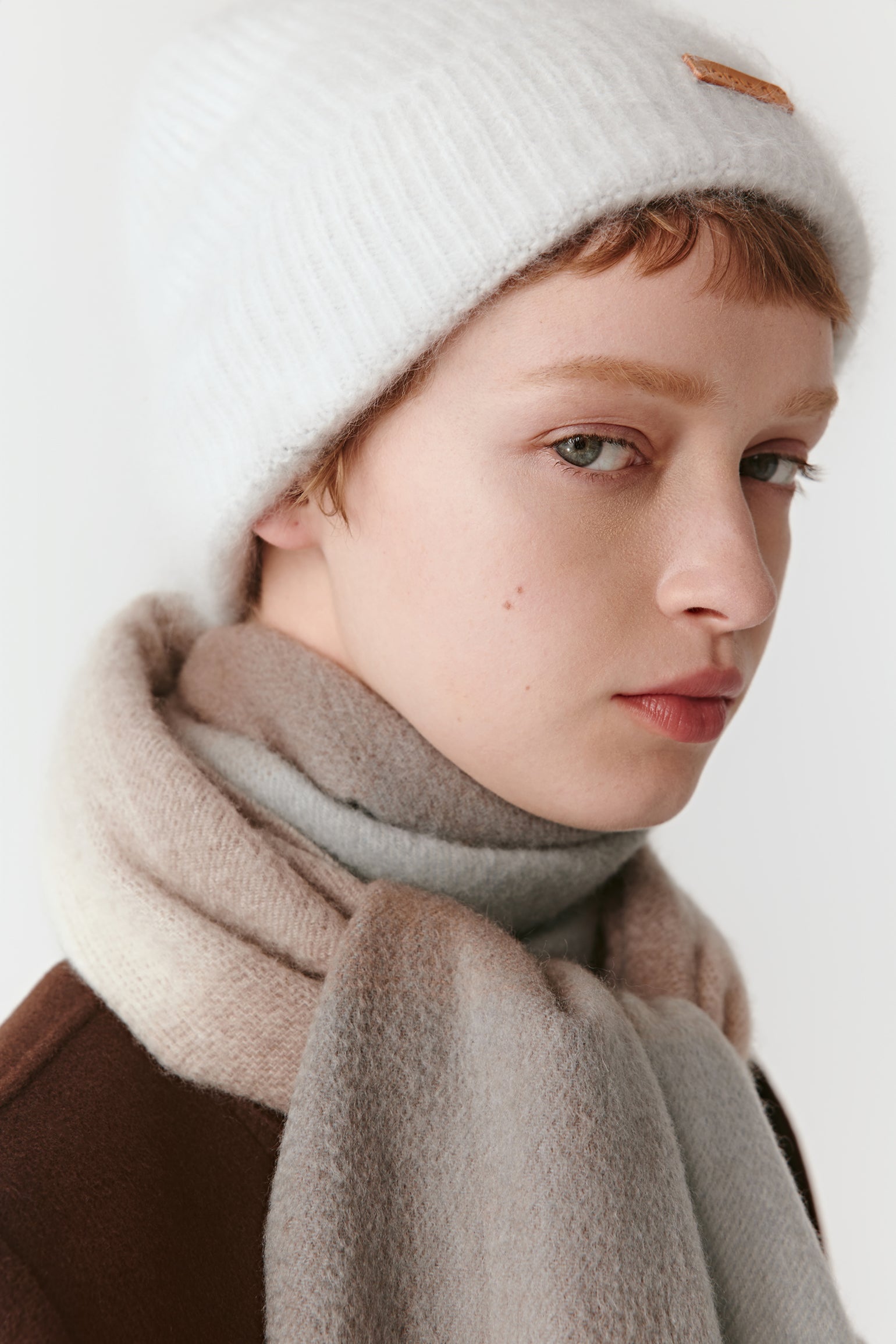 A side view of a woman wearing a gradient cashmere scarf in beige and blue tones, wrapped loosely around her neck.