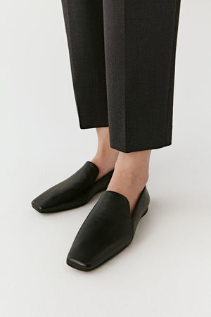 Close-up of the black nappa leather flat shoes styled with cropped trousers, showing their minimalist rounded shape.