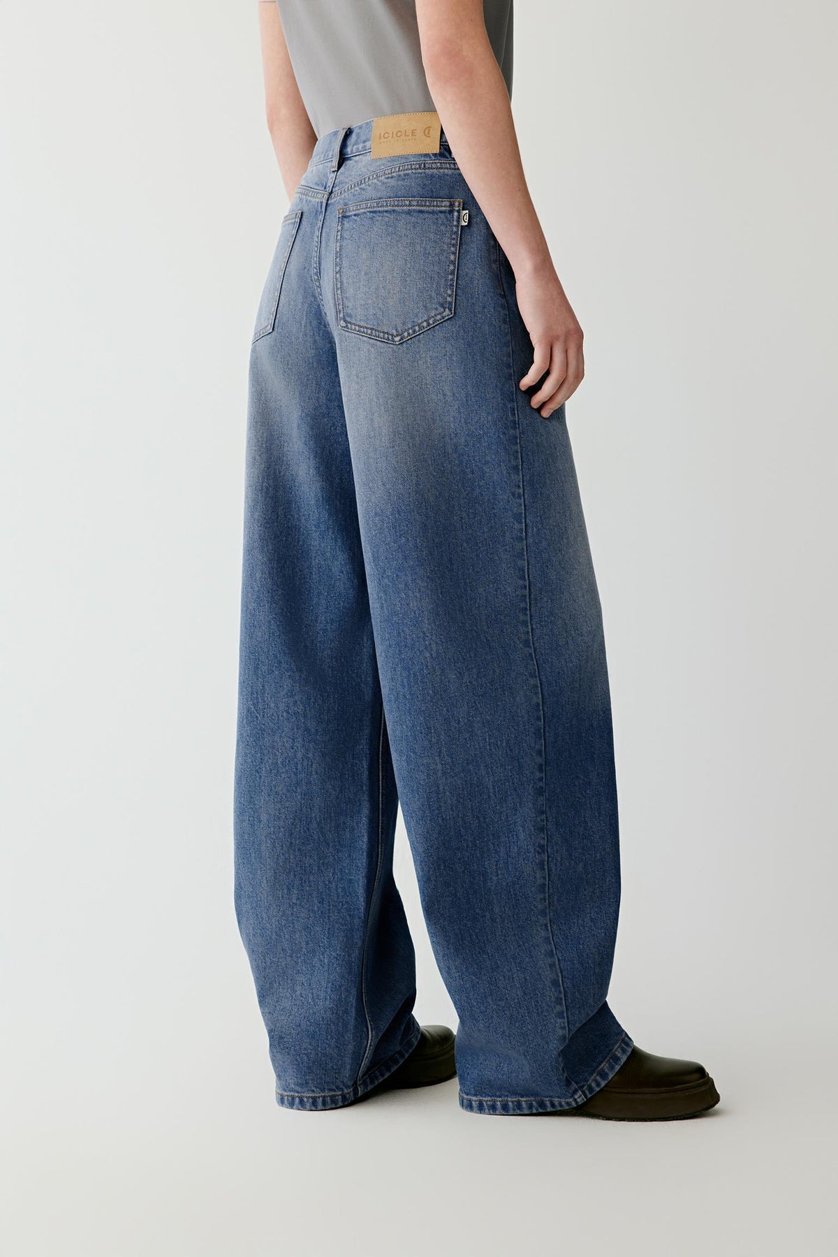 Three-quarter view showing the high-rise waist, five-pocket construction and wide-leg shape of the washed blue jeans.