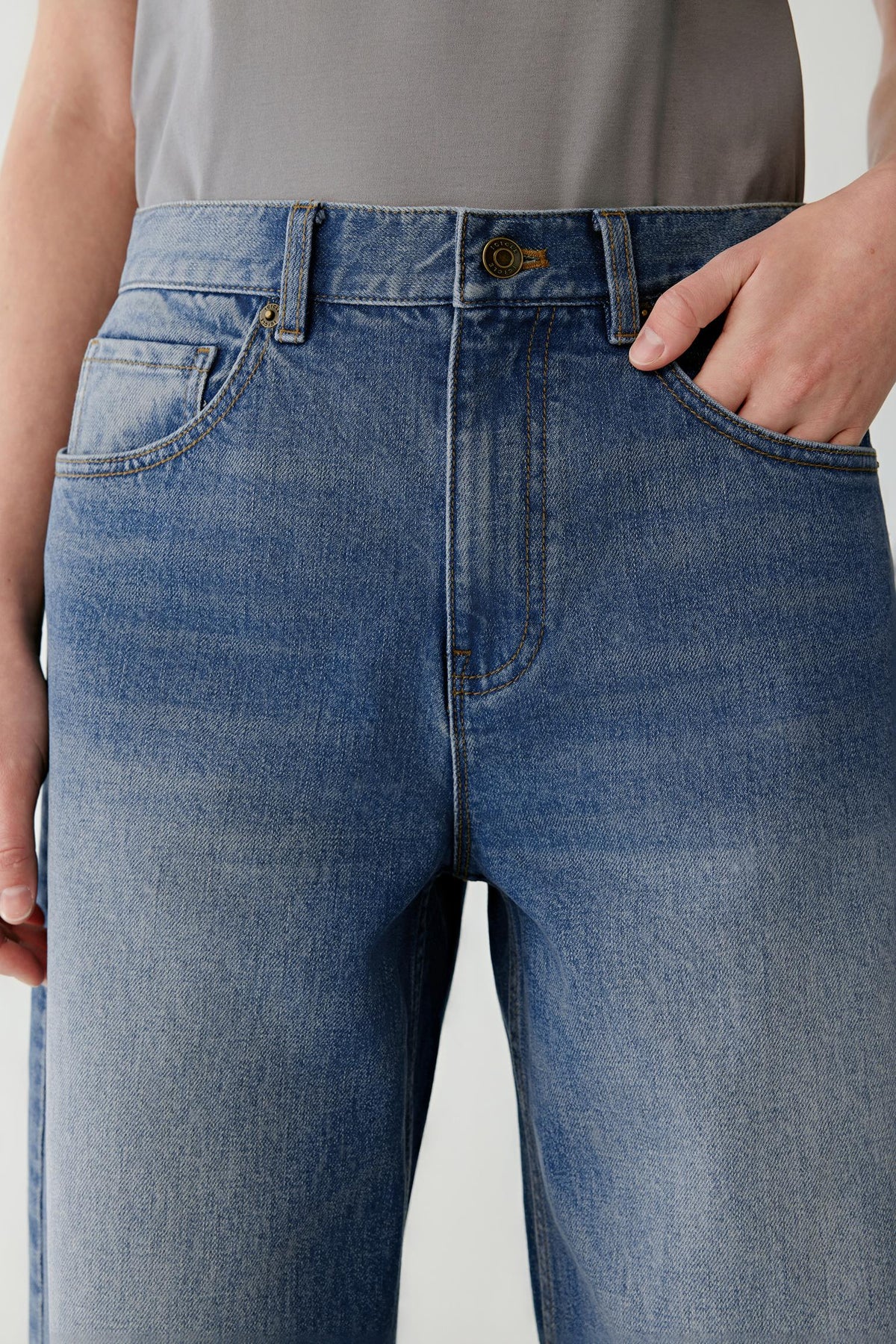 Close-up highlighting the waistband, front pockets and washed finish of the blue cotton denim jeans.